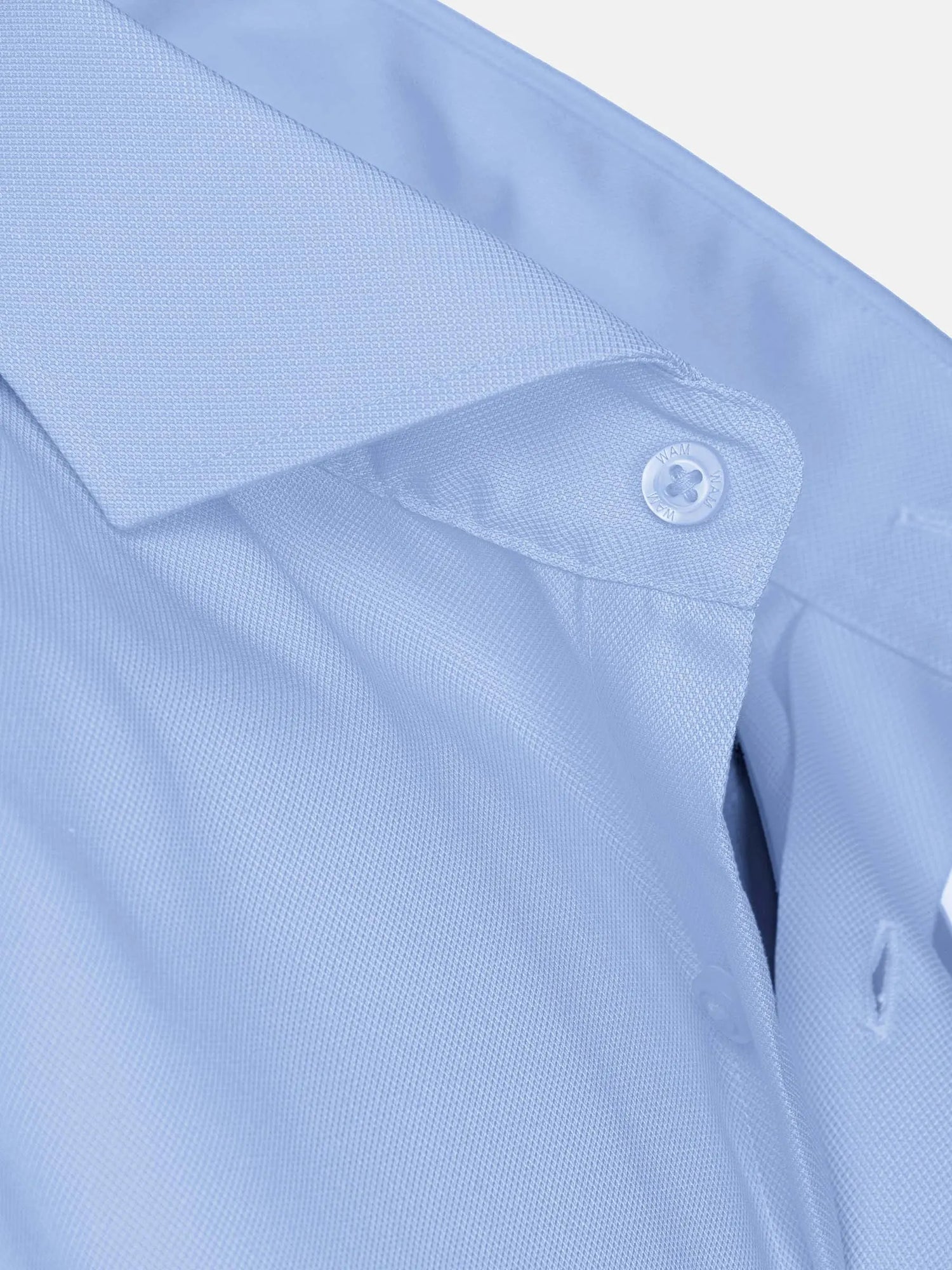 Close-up of light blue textured shirt collar with white button detail and smooth fabric – Wam Denim.