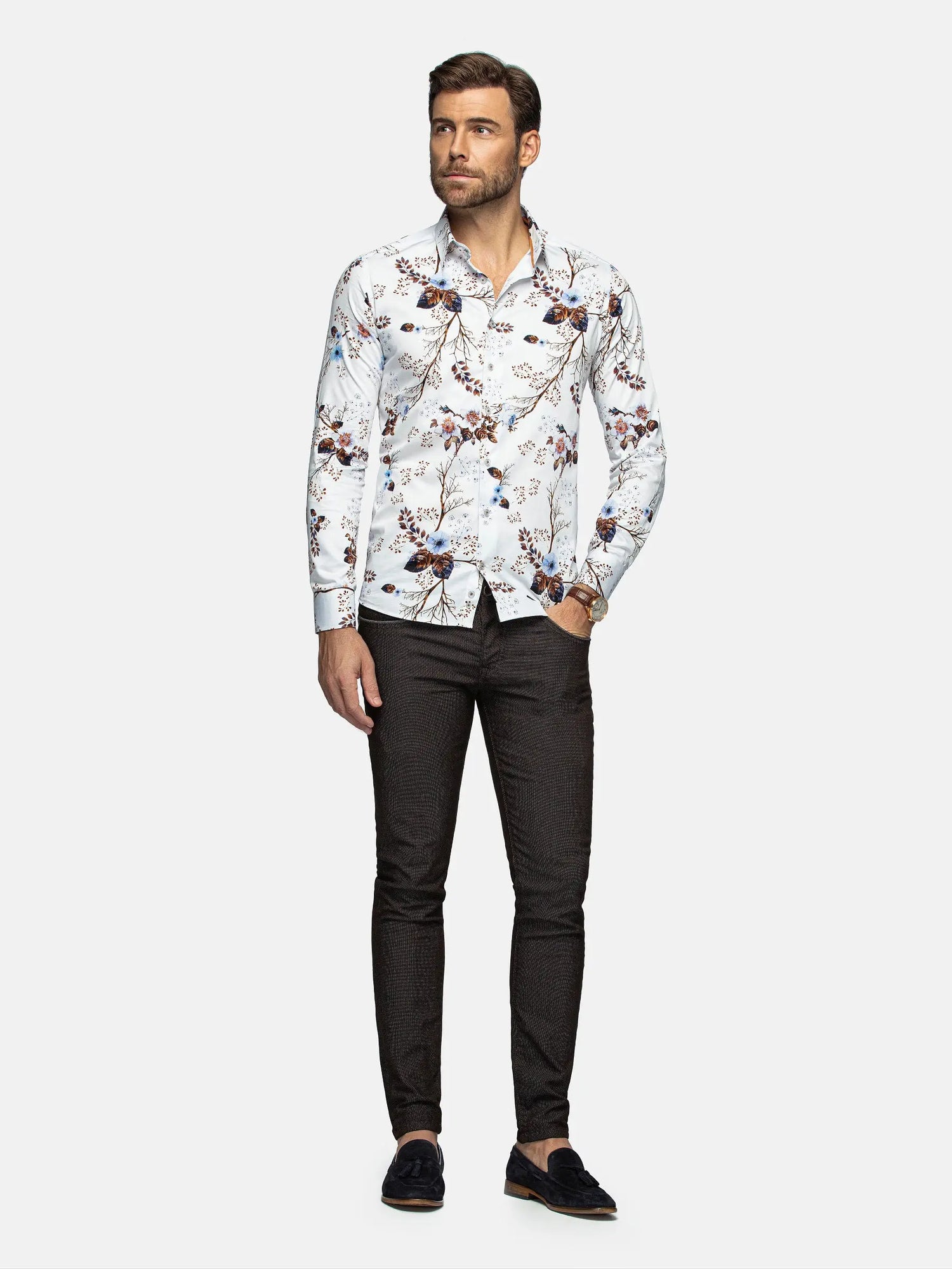 Man wearing a patterned shirt and dark pants on a white background