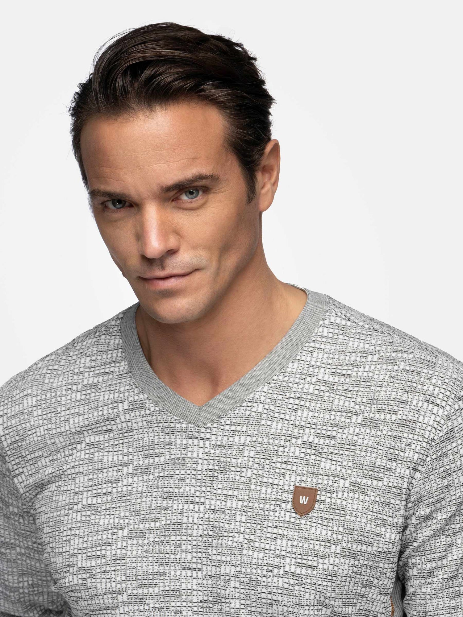 Close-up portrait of a man in a grey V-neck sweater – Wam Denim.