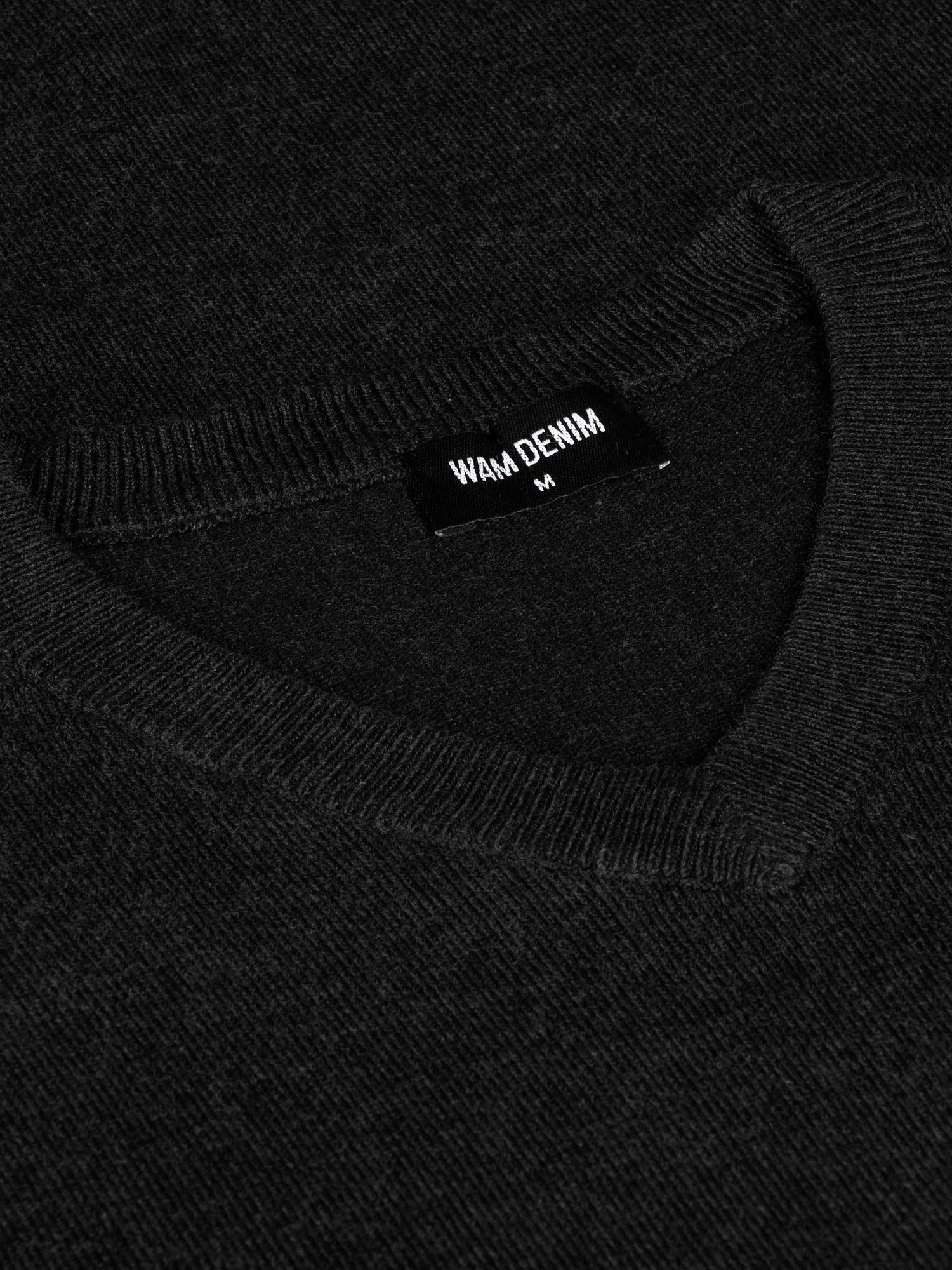 Close-up of the Wam Denim neck label on a black V-neck sweater – Wam Denim.