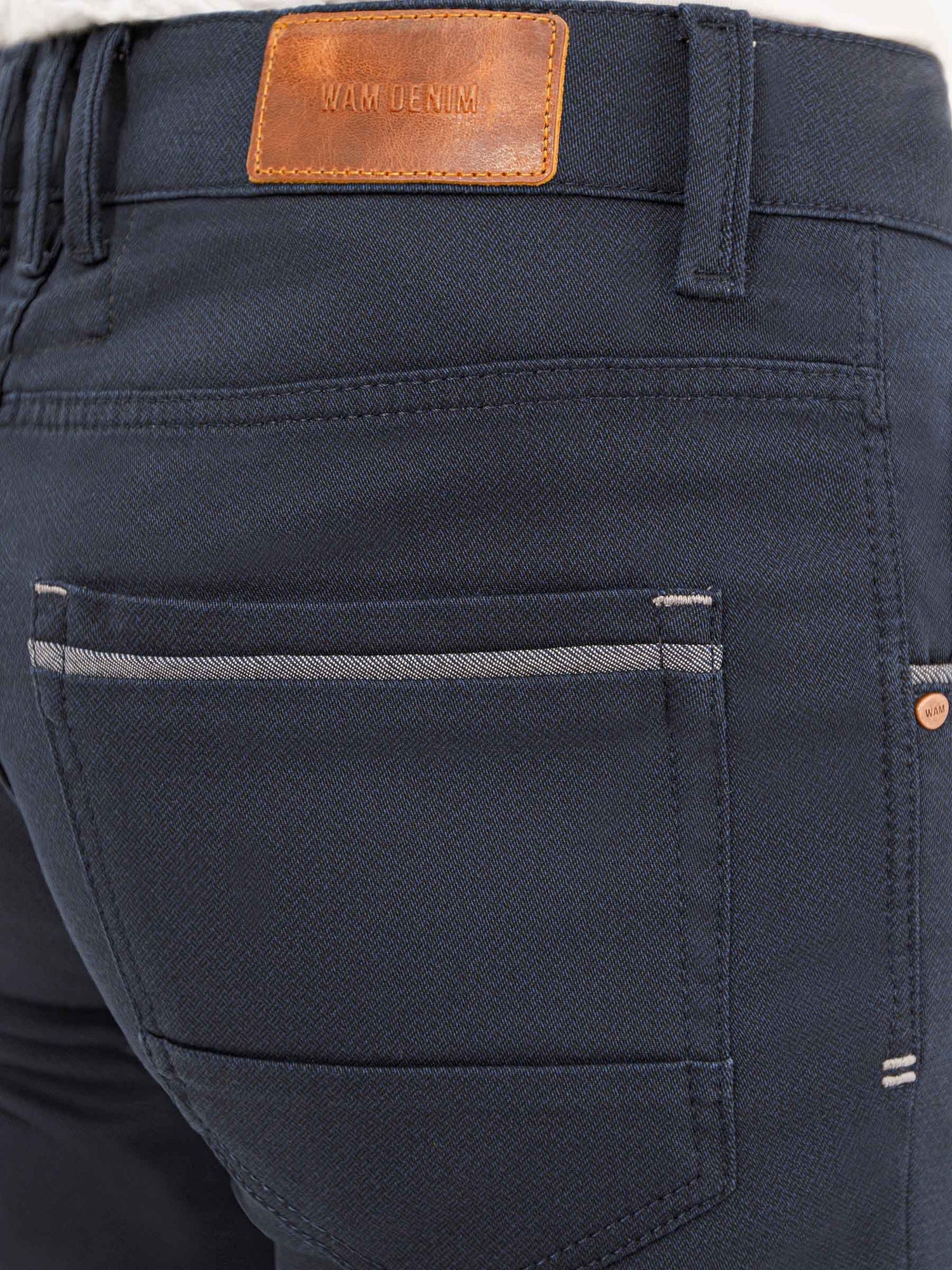 Close-up of dark blue jeans with leather label and pocket. – Wam Denim.