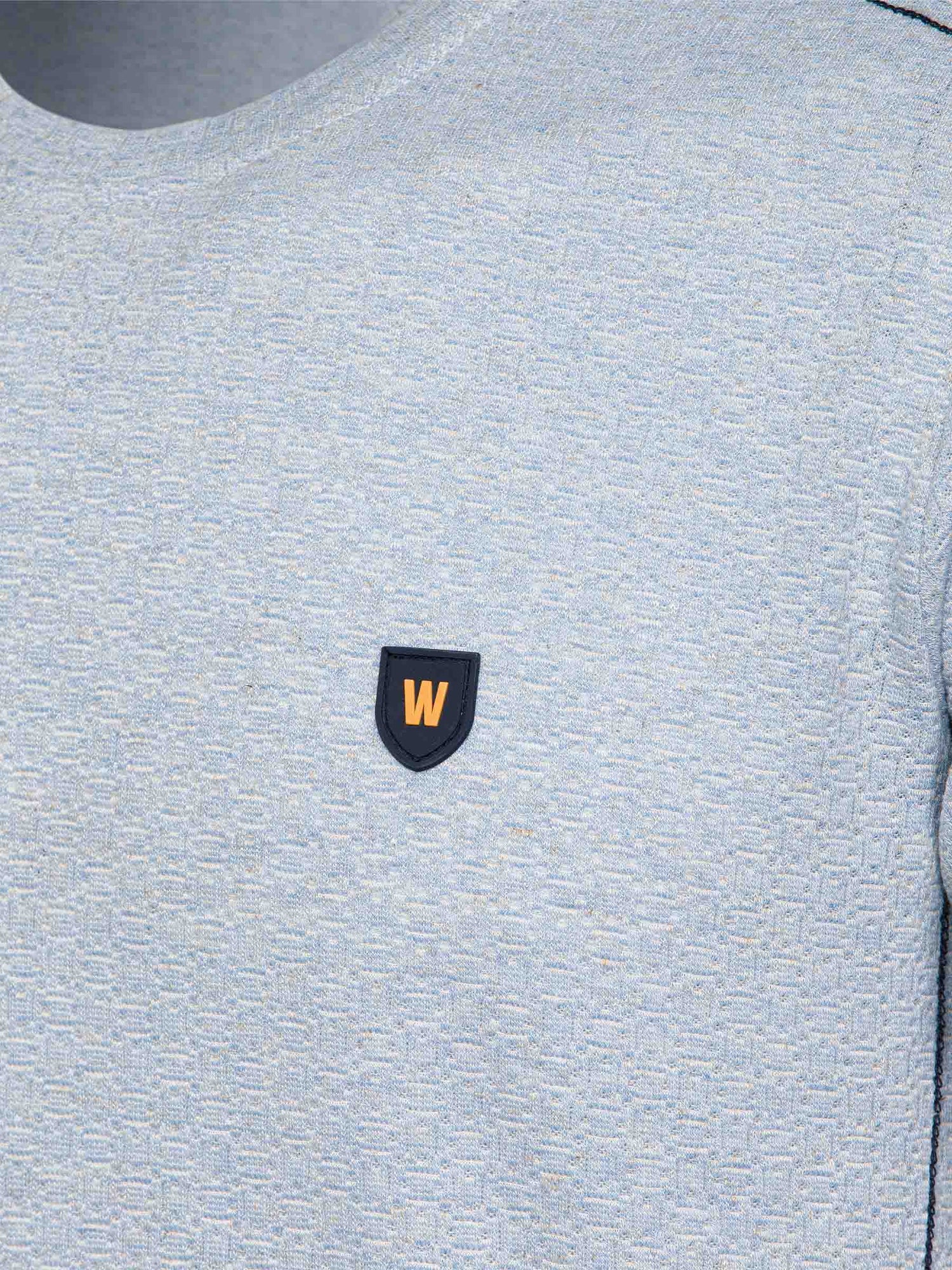 Close-up of the W-shield logo on the blue t-shirt – Wam Denim.
