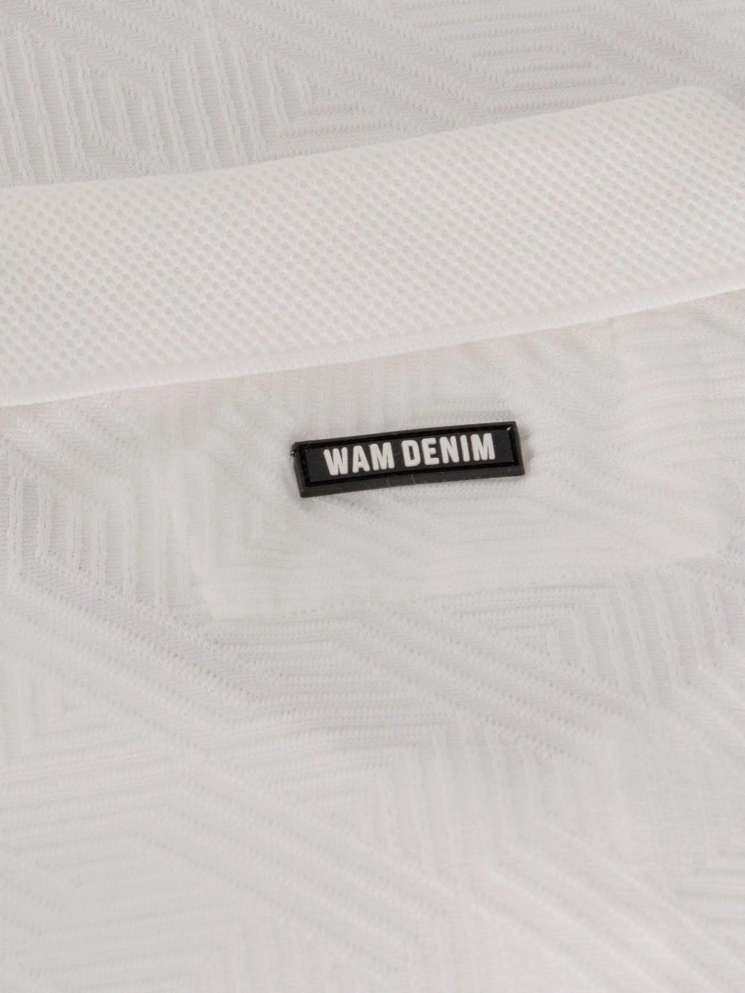 Close-up of the Wam Denim logo on the white polo shirt collar – Wam Denim.