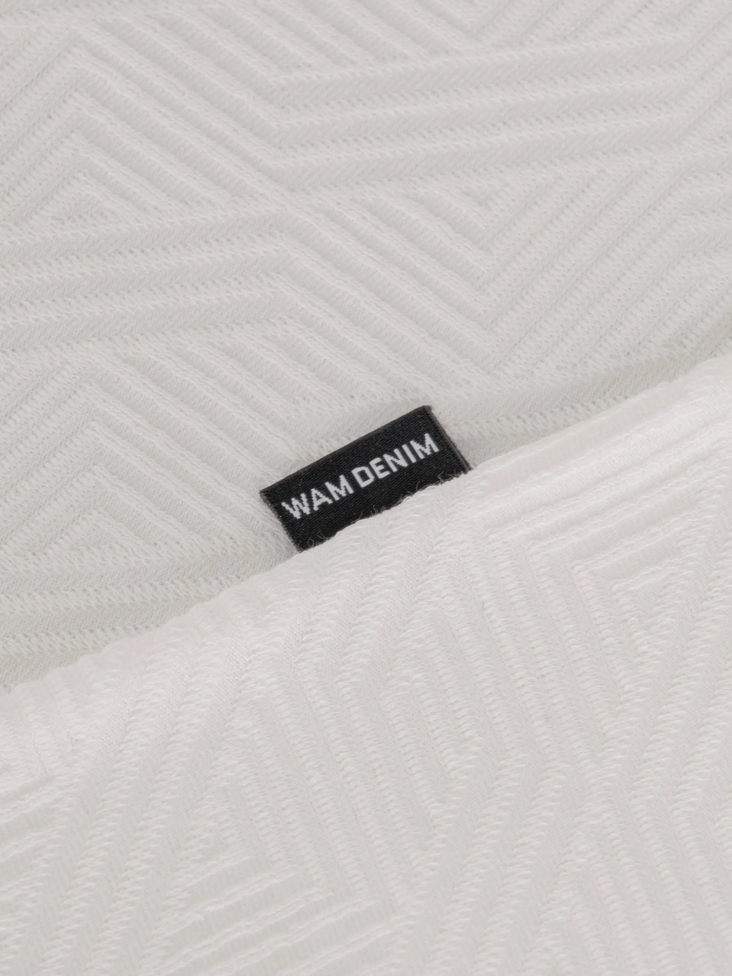 Close-up of the Wam Denim label on the textured white polo – Wam Denim.