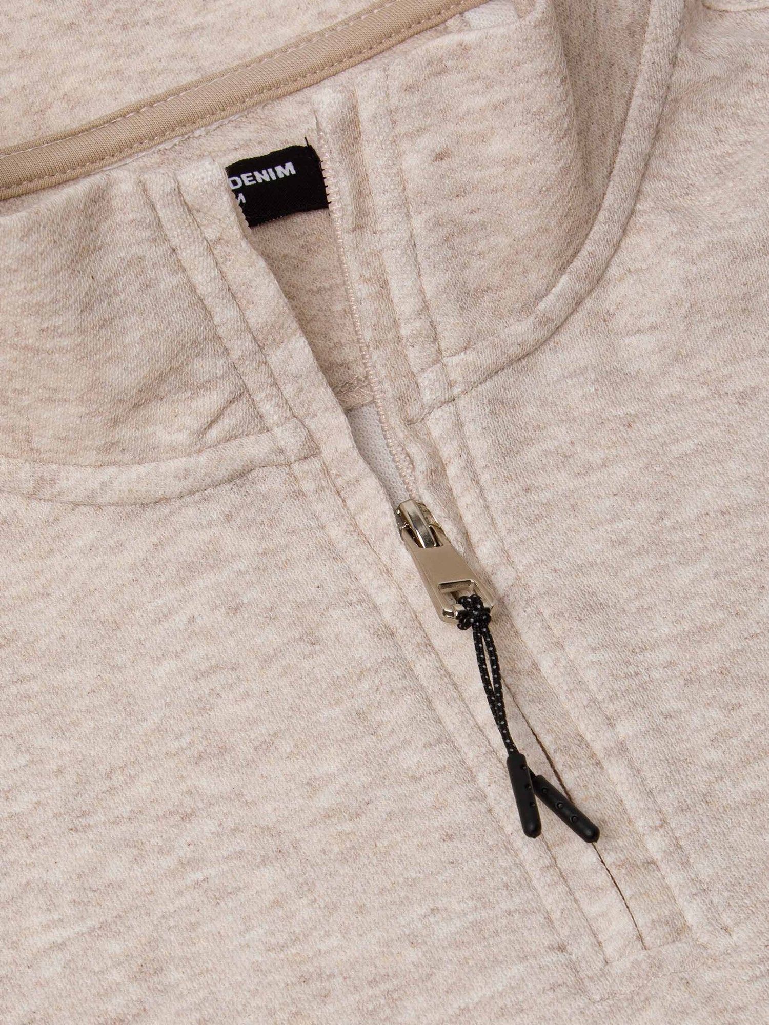 Close-up of a beige fleece sweater with a zipper and ' Wam Denim' brand label.
