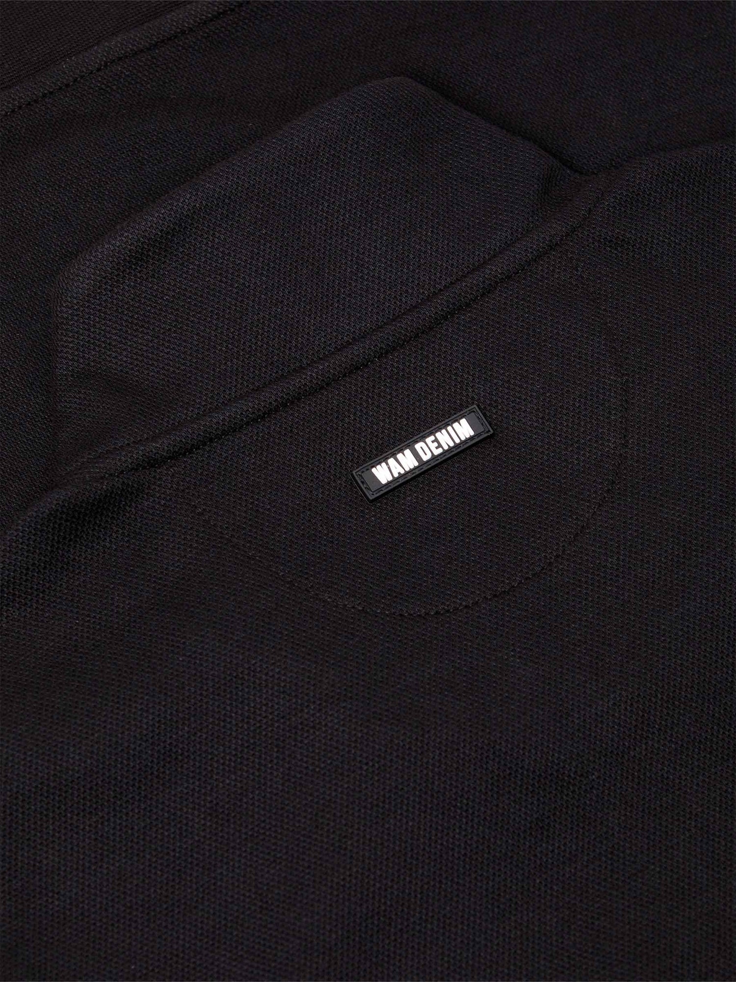 Close-up of black textured sweater fabric with Wam Denim logo tag on the back – Wam Denim.