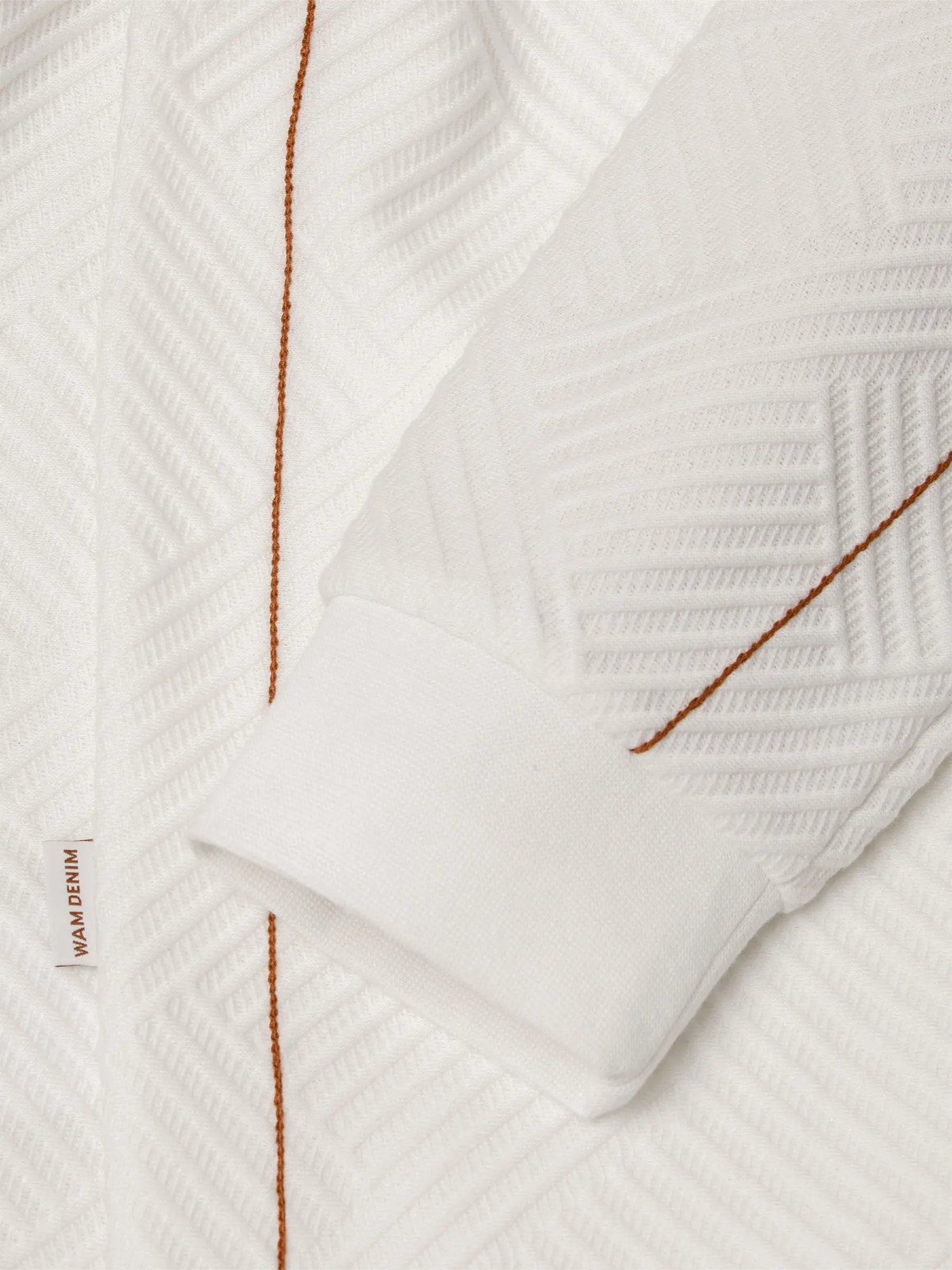 Close-up of white textured sweatshirt sleeve with brown stitching and cuff detail – Wam Denim.