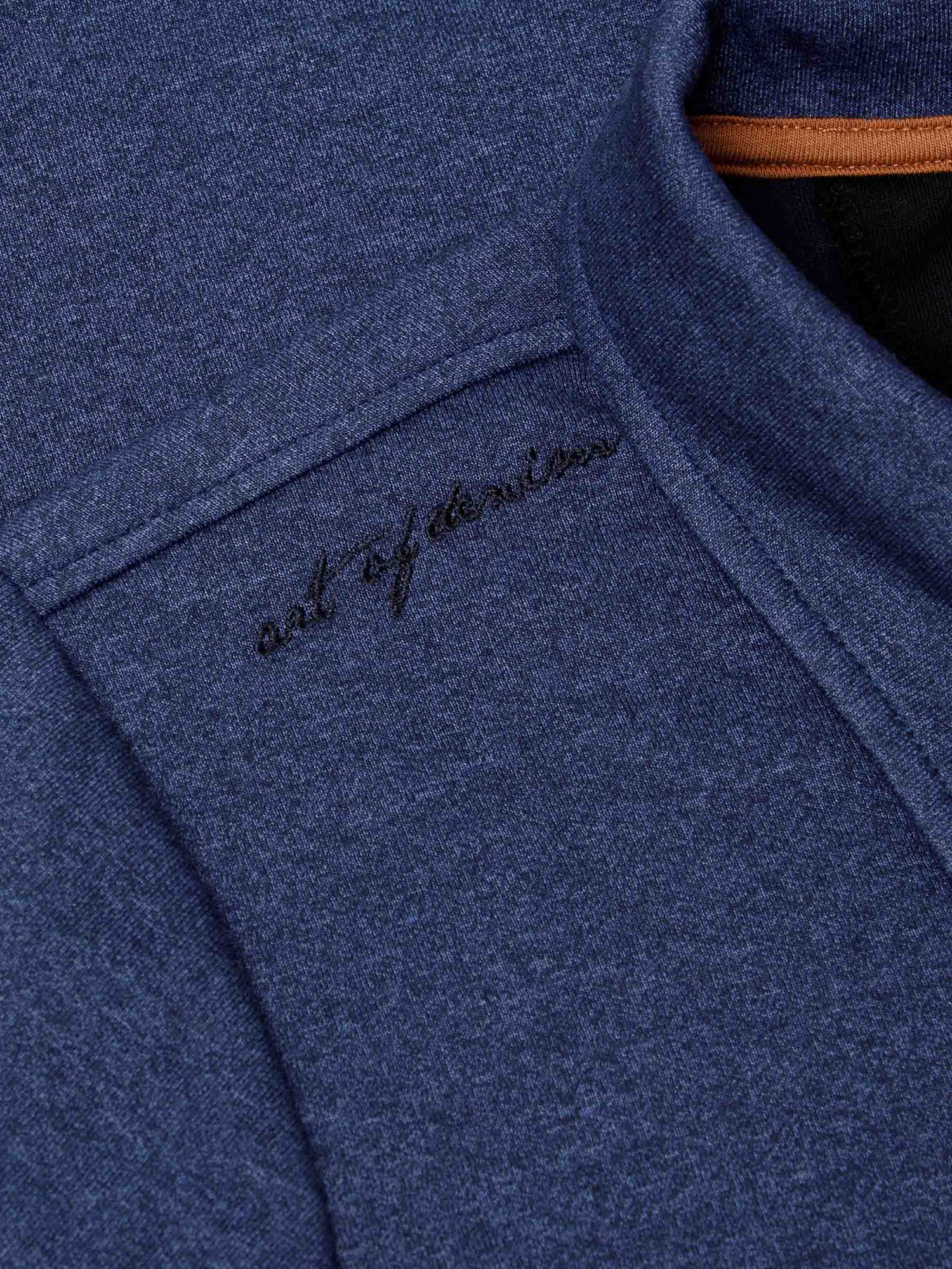 Close-up of embroidered “art of denim” detail on light indigo fabric near collar – Wam Denim.