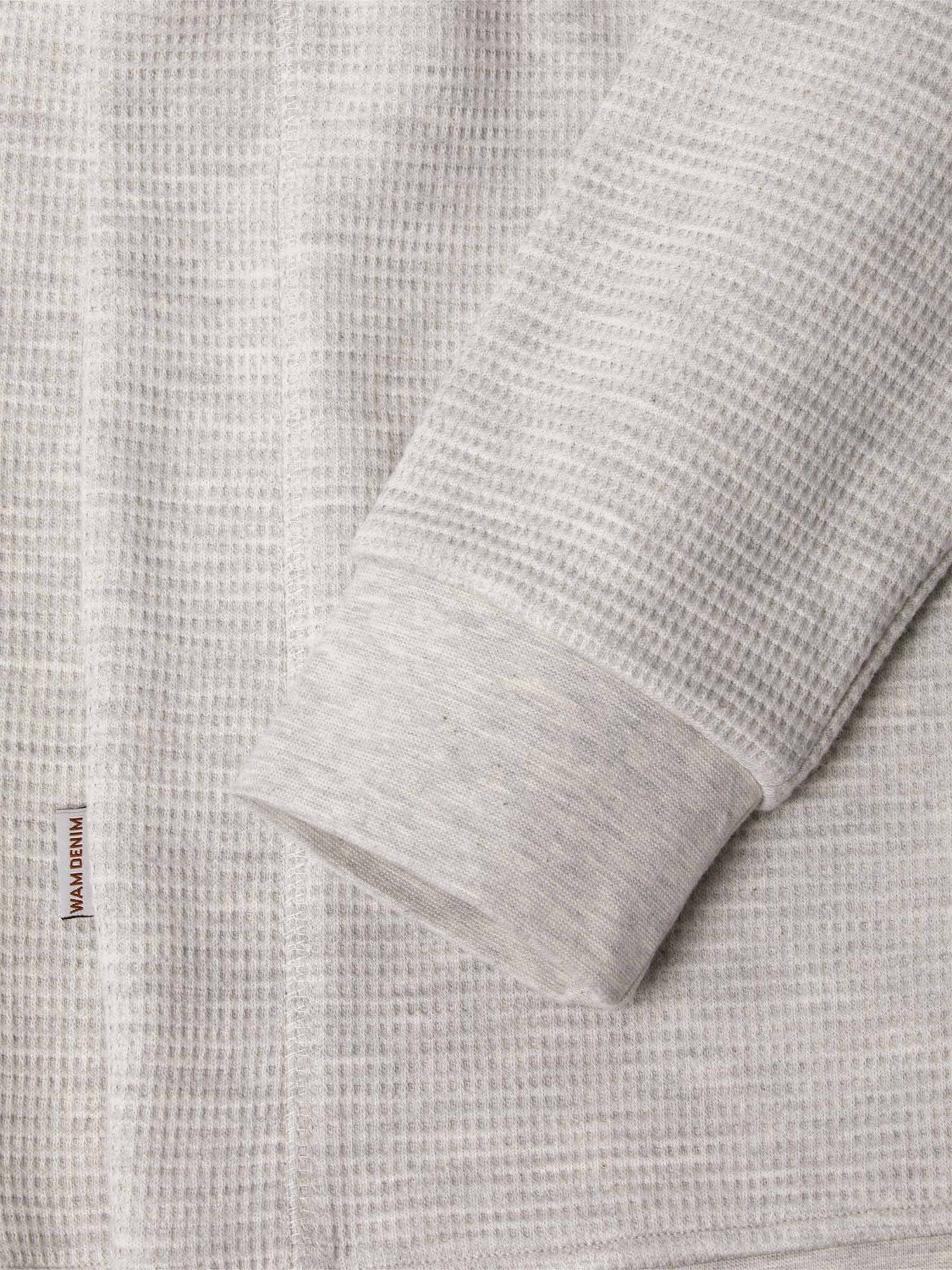 Close-up of light grey waffle-textured sweatshirt sleeve and hem with logo tag – Wam Denim.