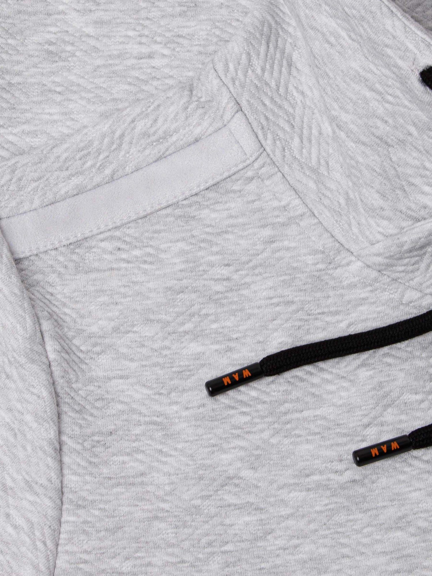 Close-up of light grey textured hoodie pocket with black drawstrings featuring Wam branding – Wam Denim.