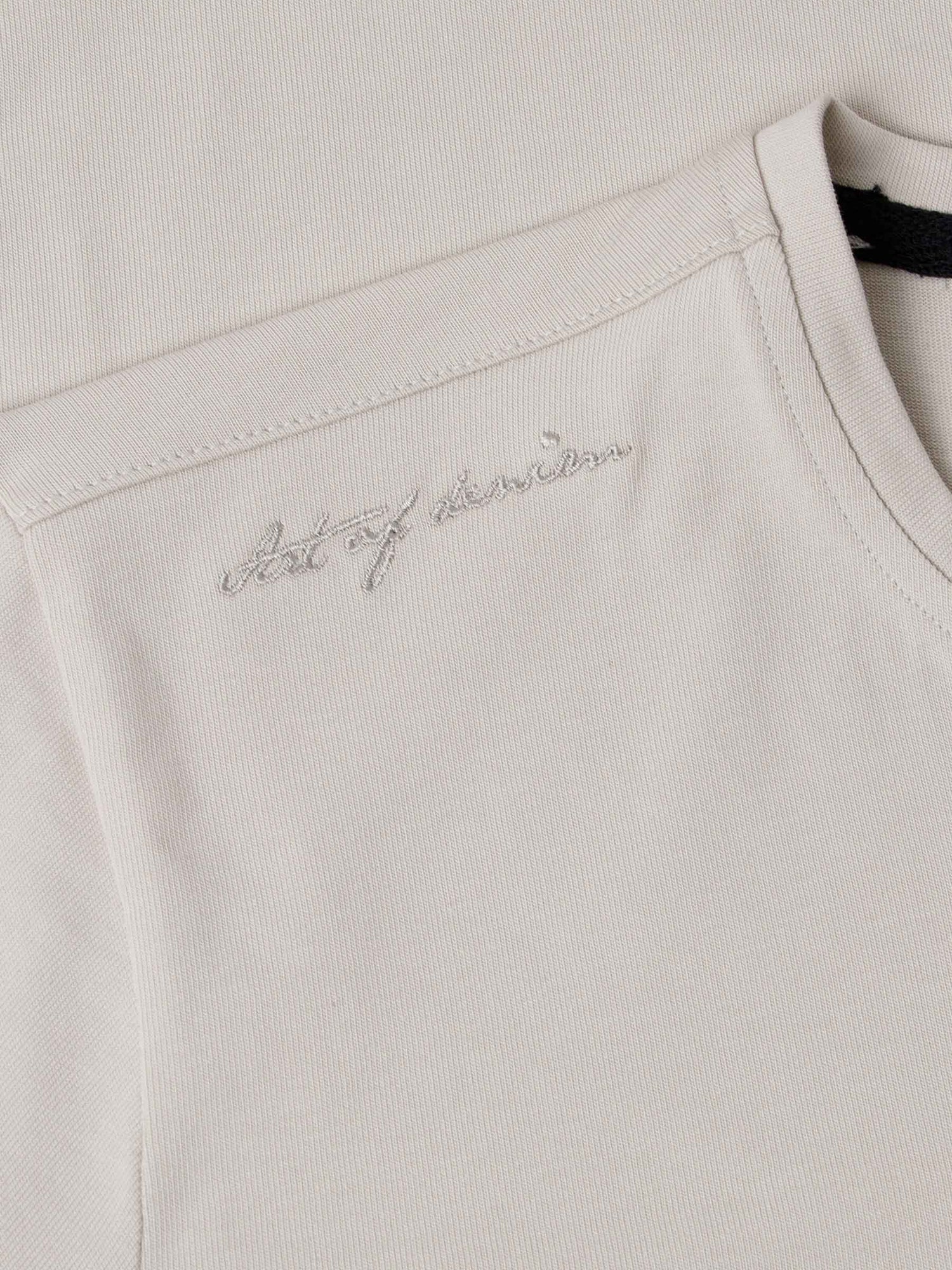 Close-up of The Fervor Light Beige Sweater shoulder embroidery reading “Art of Denim” – Wam Denim.