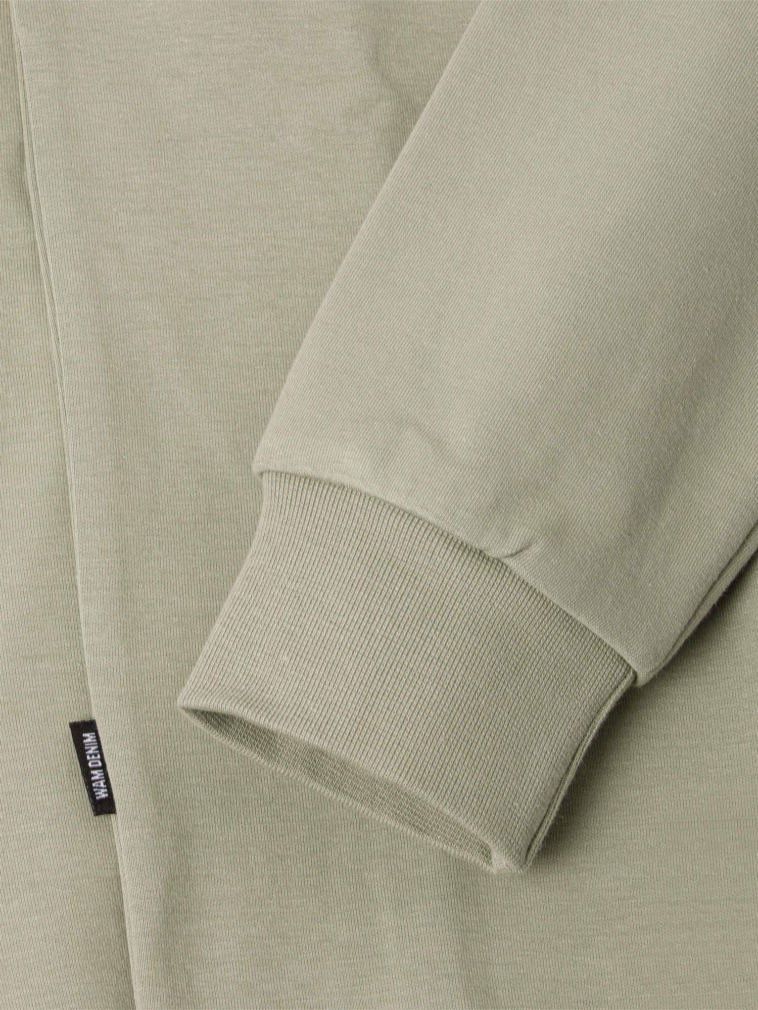 Close-up of a light green sweater with a brand label on the sleeve.