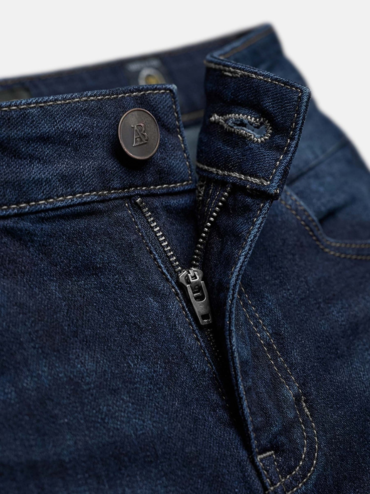 Close-up of navy denim jeans showing button closure, zipper fly, and durable stitching.