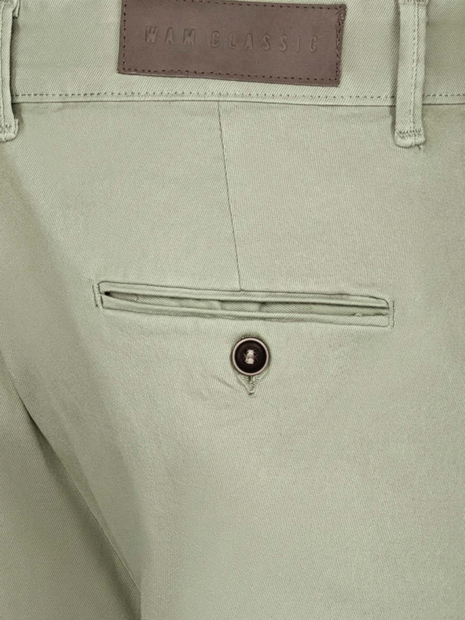 Close-up of light green chino pants showing rear pocket, button detail, and fabric texture.