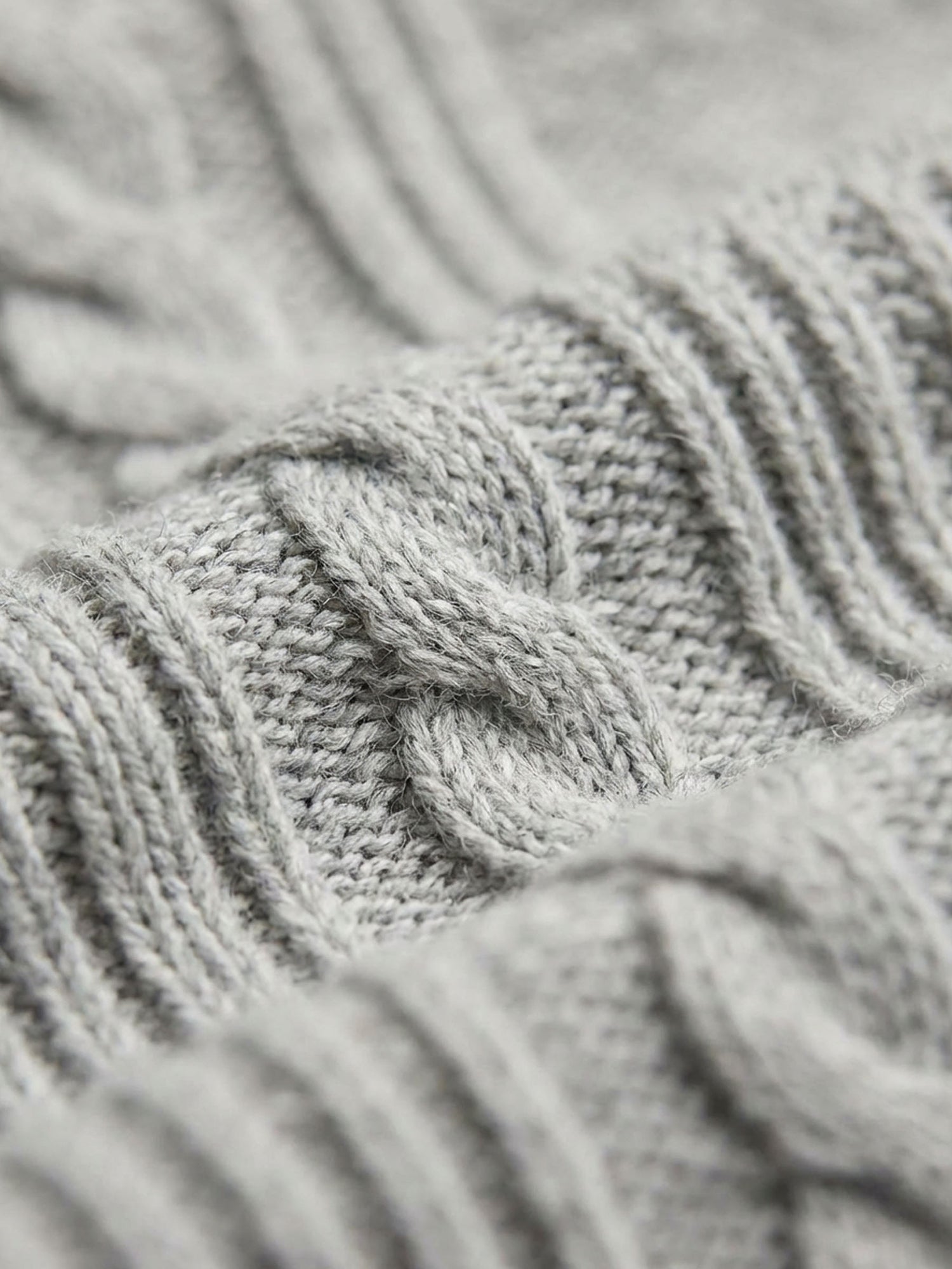 Close-up of light grey knit sweater fabric showing detailed cable-knit texture.