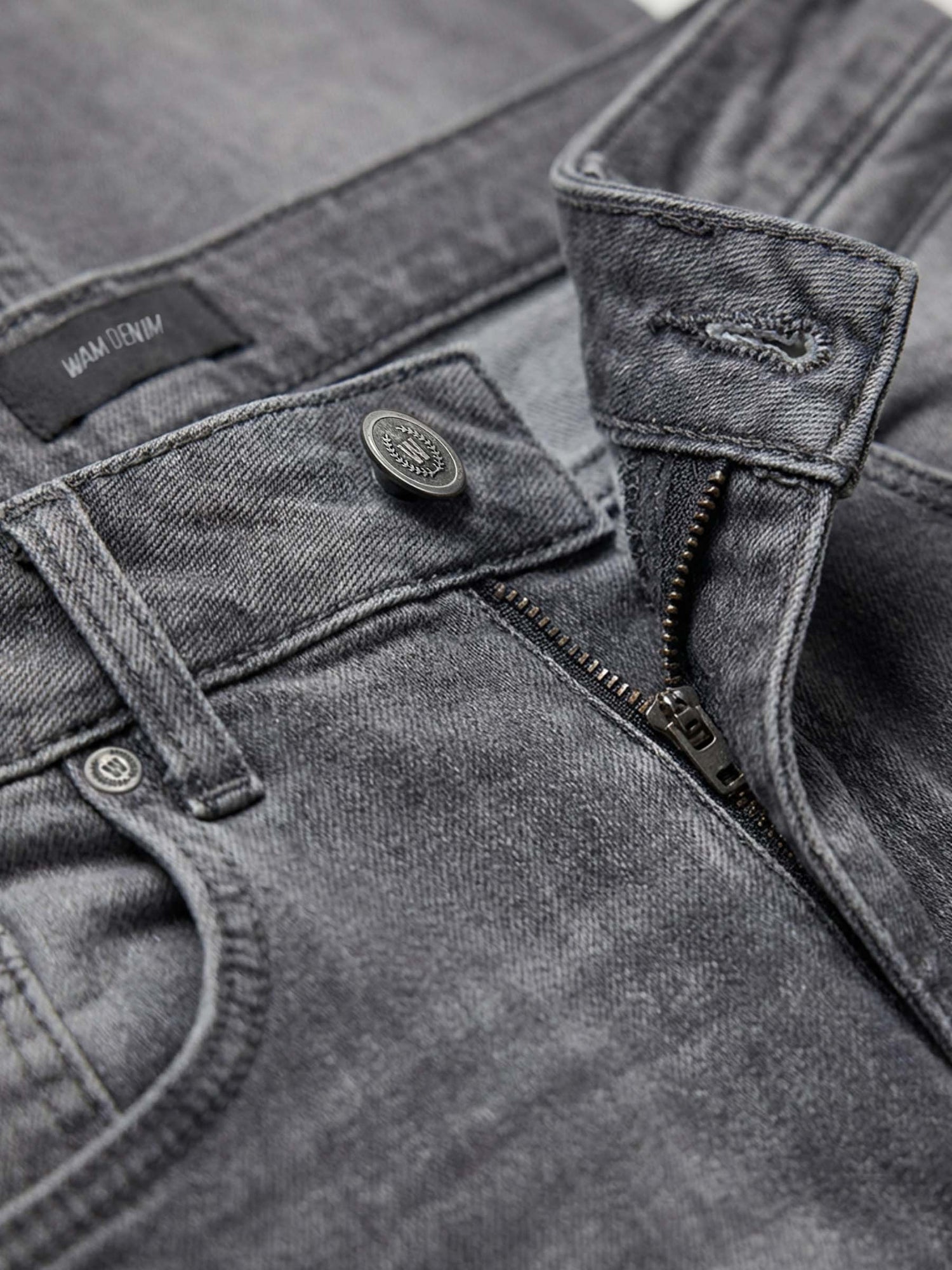Close-up of grey jeans waistband with zip fly, button closure, and premium denim texture.