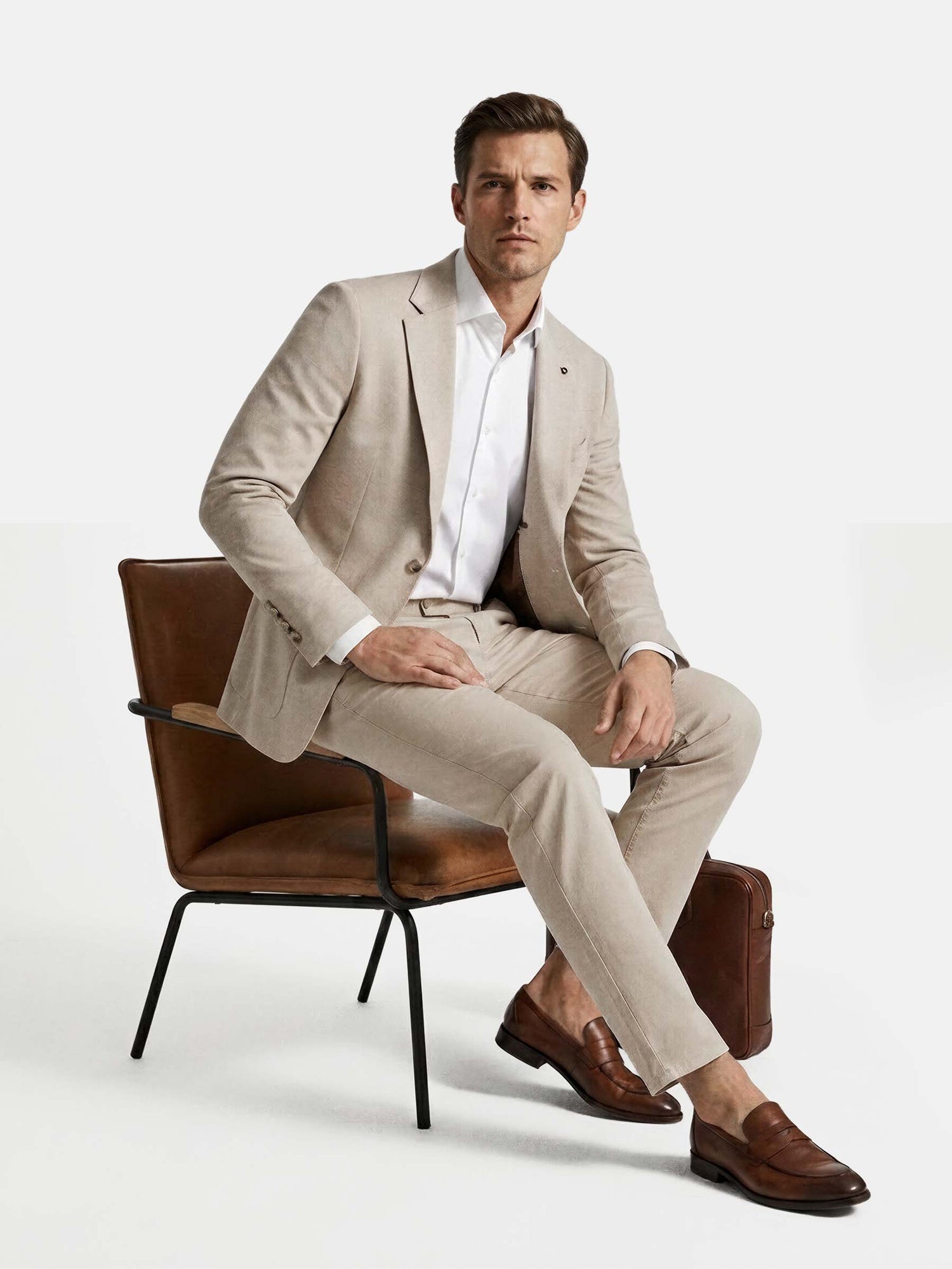 Model seated wearing beige blazer styled with white shirt and tailored trousers