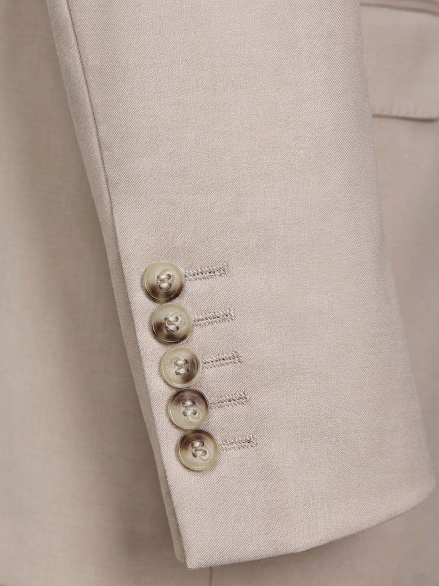 Close-up of beige blazer sleeve with refined button cuff detailing