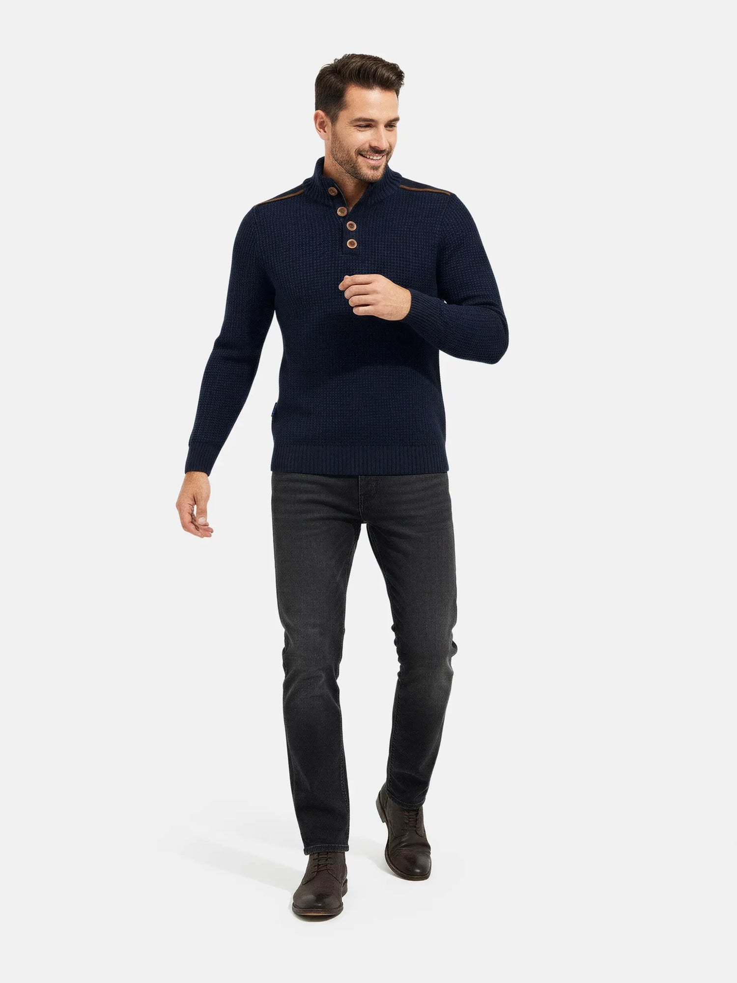 Full-body view of a man wearing an indigo navy textured knit sweater with dark jeans.