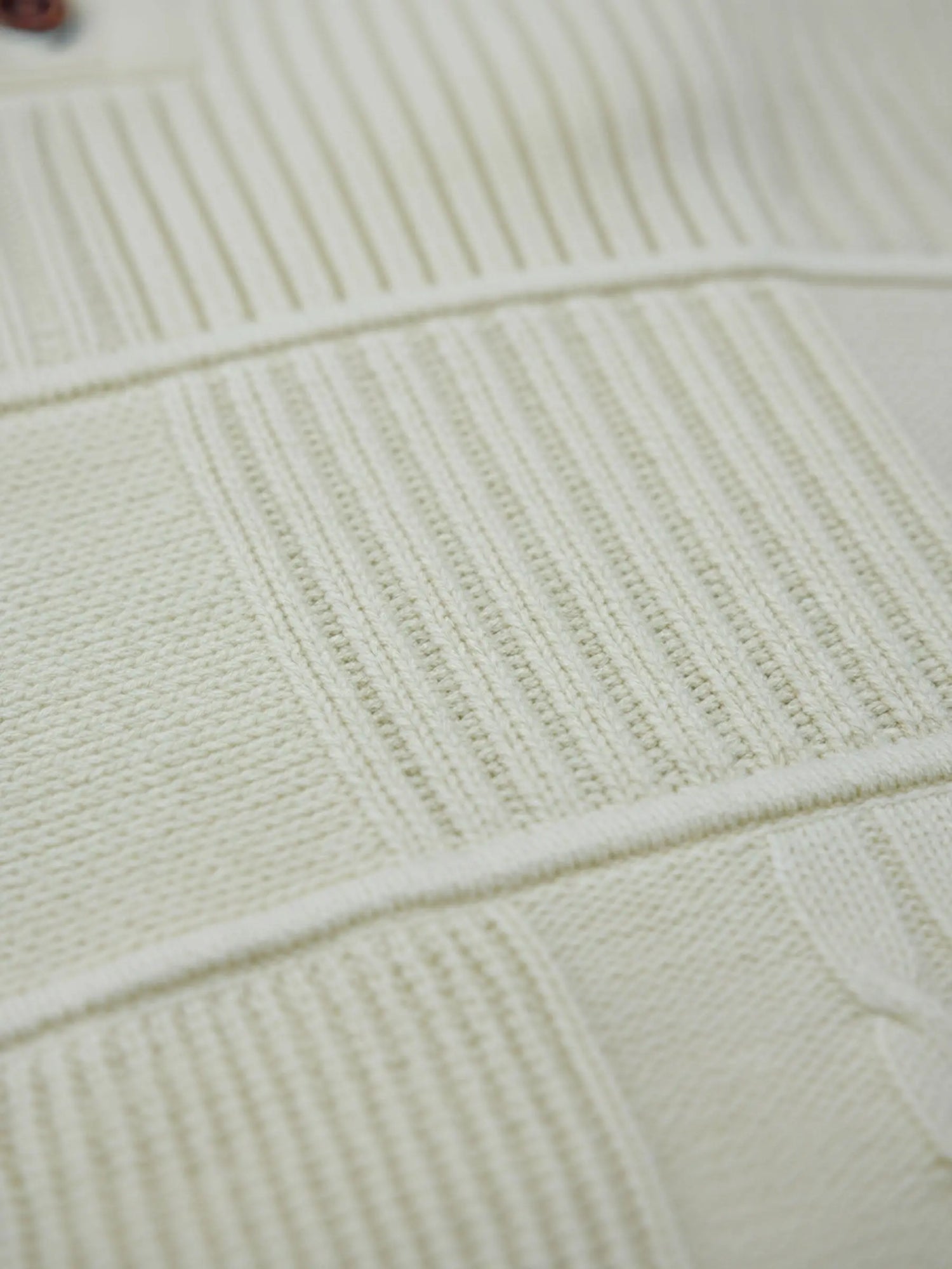 Close-up of off-white knit sweater fabric showing textured ribbed and patterned details.