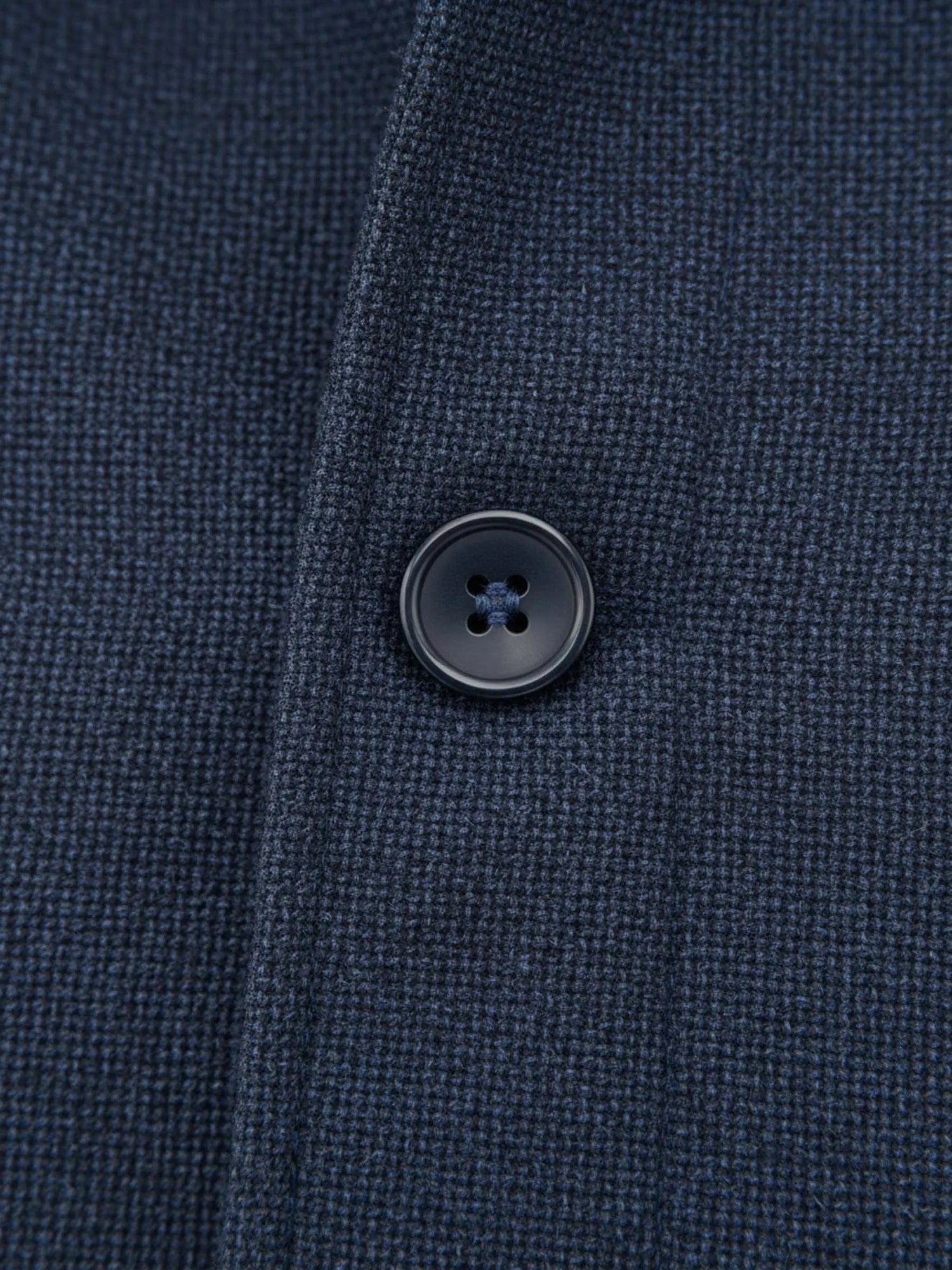 Close-up of light navy trenchcoat fabric showing textured weave and black button detail.