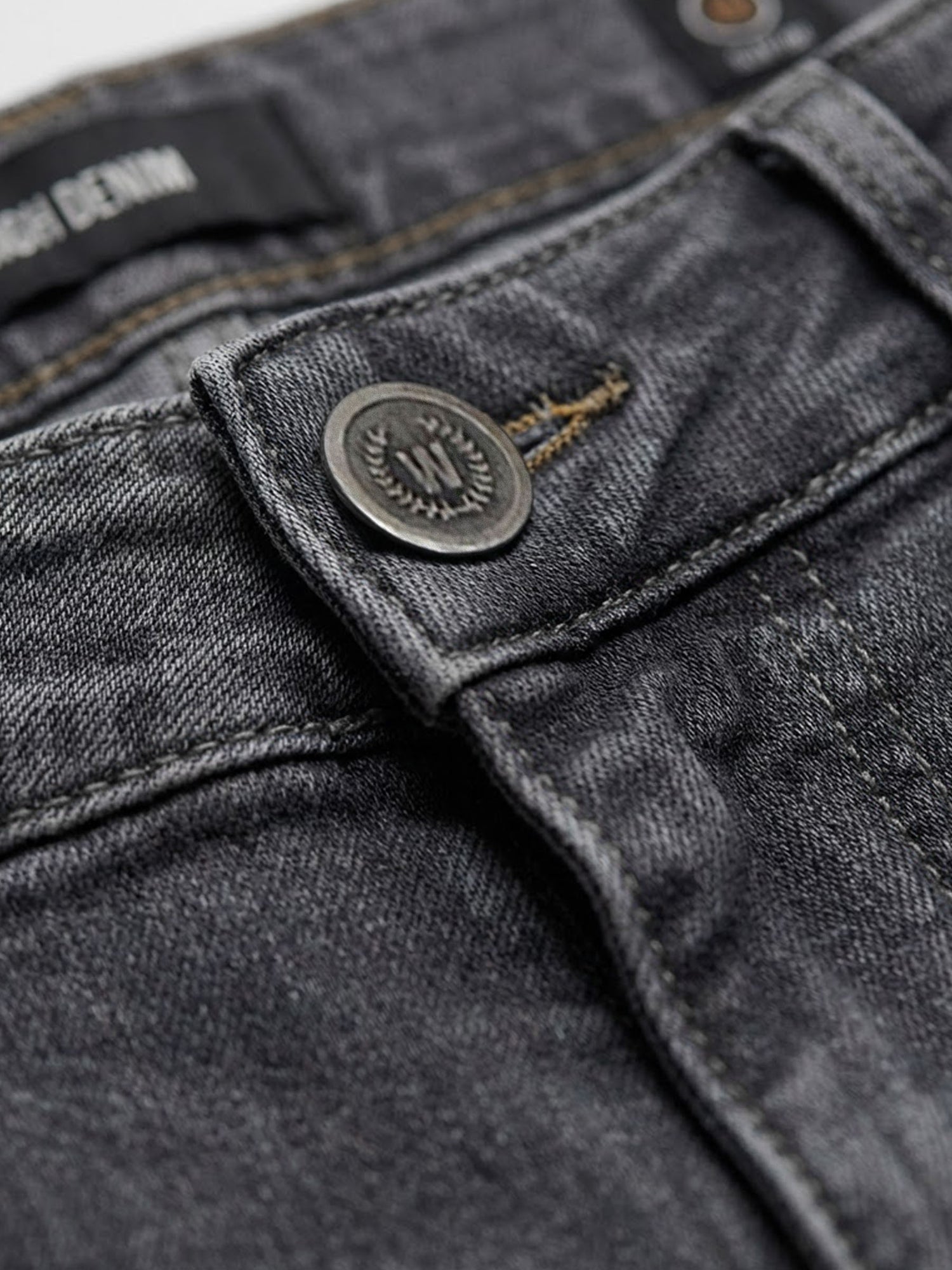 Close-up of grey denim jeans button and waistband stitching detail.