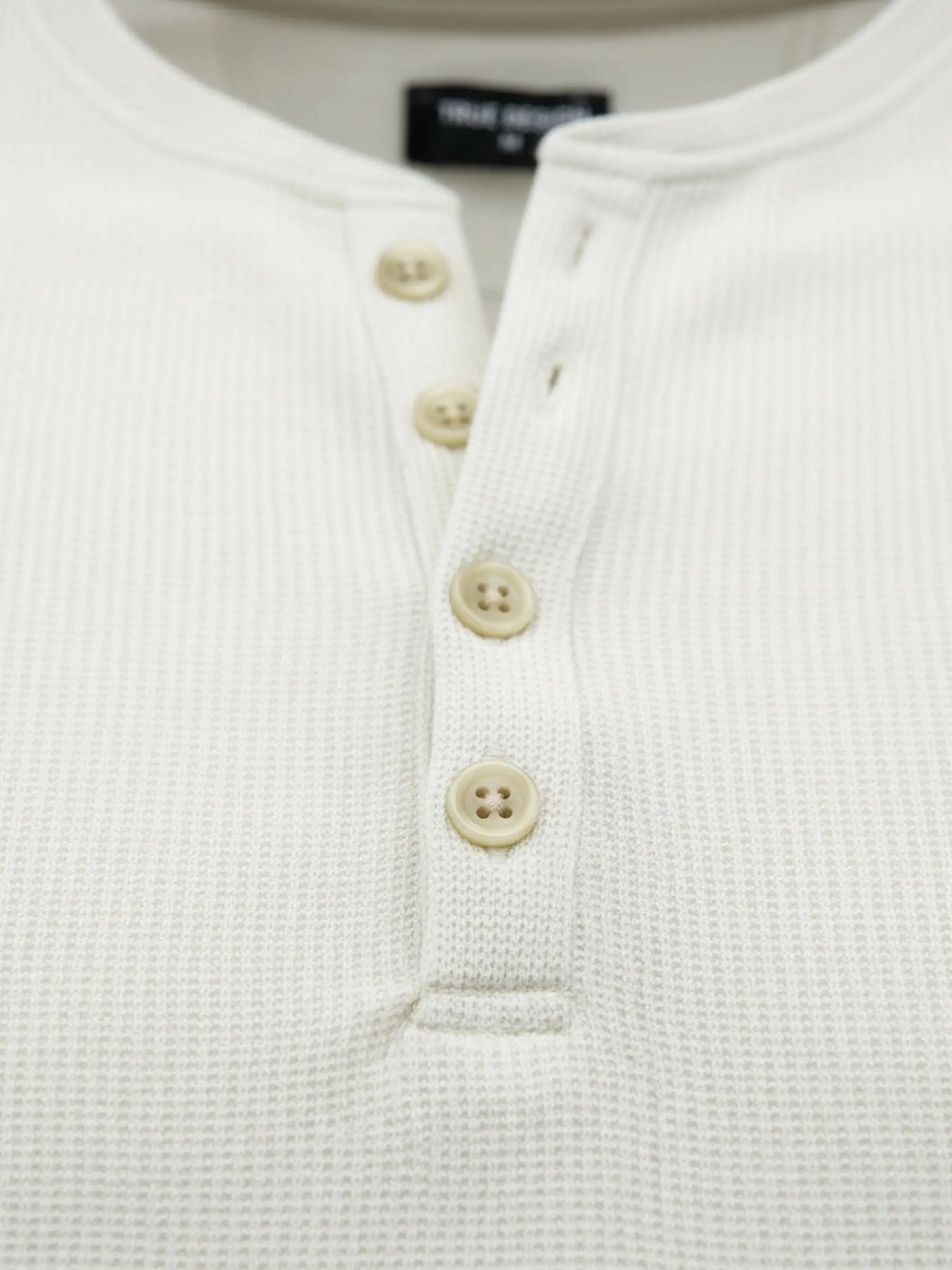 Close-up of off-white sweater buttons and textured waffle knit fabric.