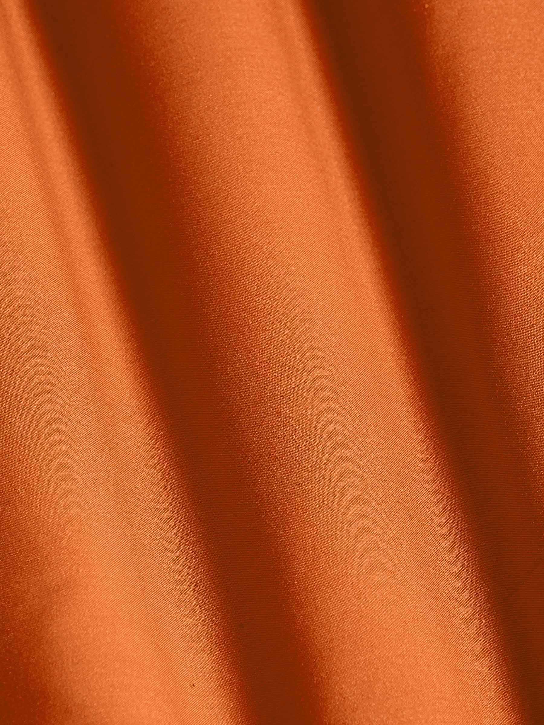 Close-up of smooth orange fabric highlighting soft texture and premium quality – Wam Denim.