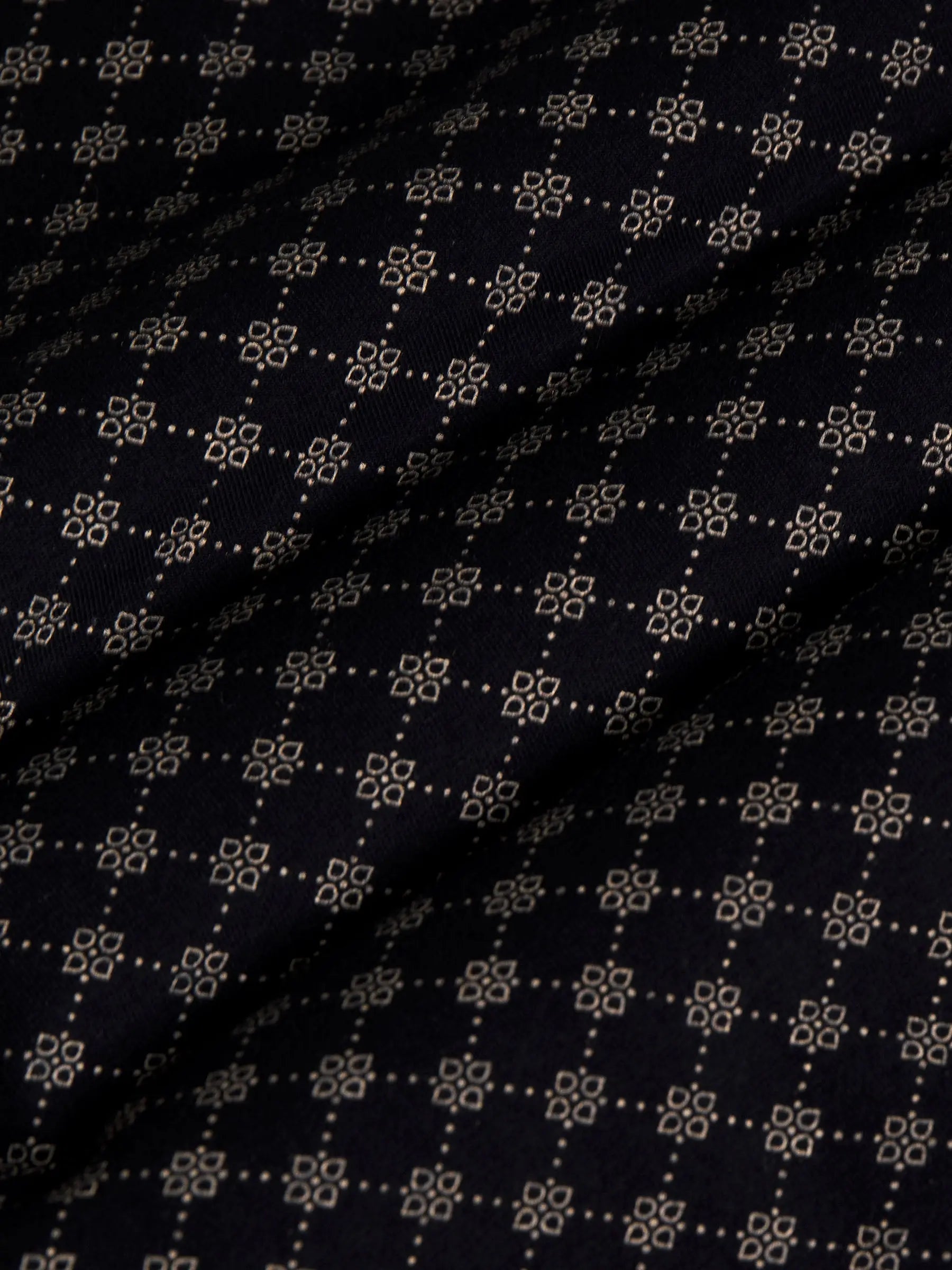 Close-up of black fabric with beige geometric pattern showing soft textured weave – Wam Denim.