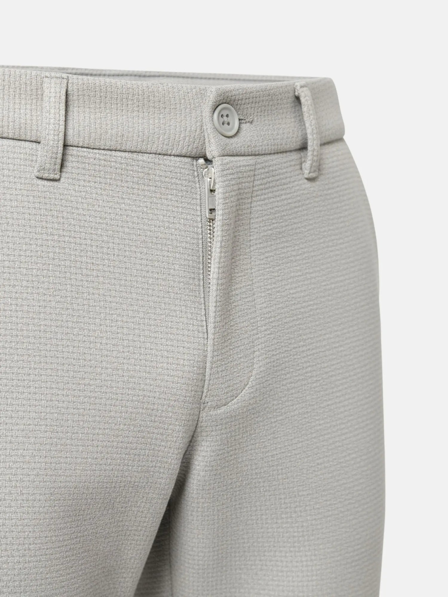 Close-up of light grey pantalon showing textured fabric, button closure, and zipper detail.