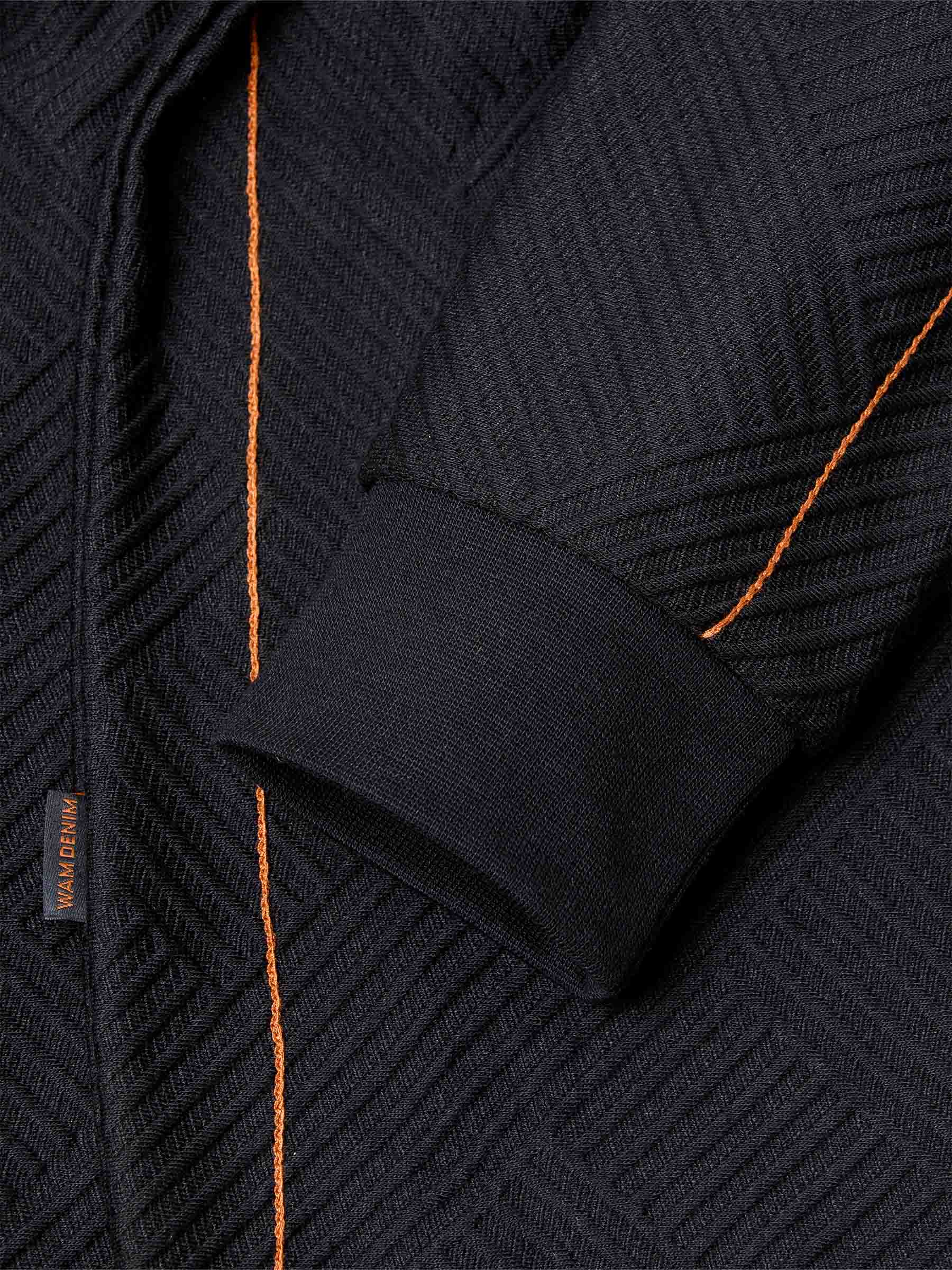 Close-up of sleeve and orange stitch detailing on black textured fabric – Wam Denim.