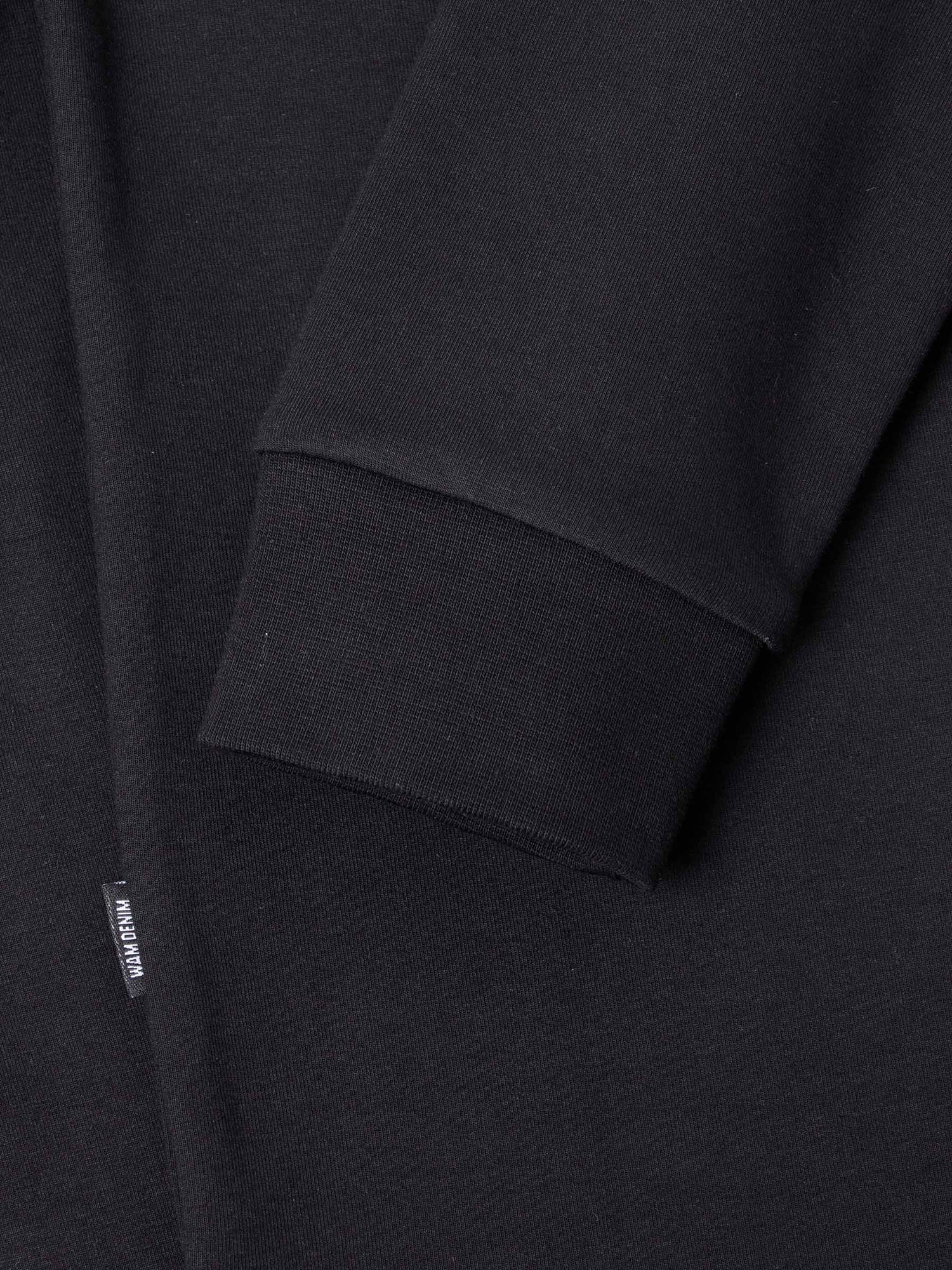 Close-up of The Zeal Black Sweater sleeve cuff showing ribbed finish and woven label – Wam Denim.