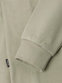 Close-up of a light green sweater with a brand label on the sleeve.