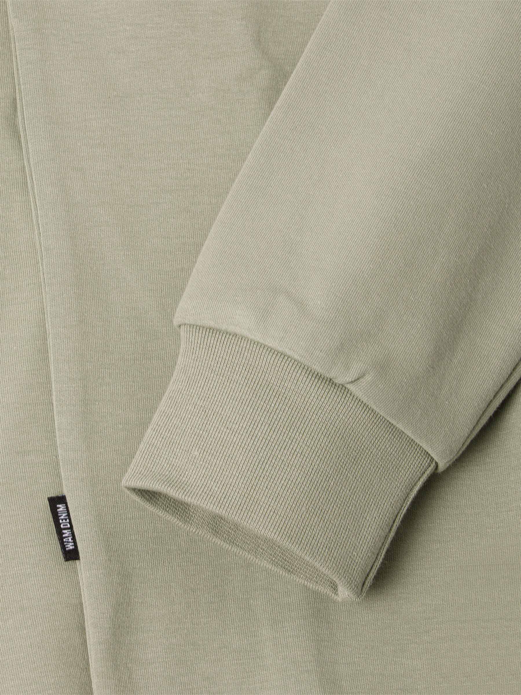 Close-up of a light green sweater with a brand label on the sleeve.