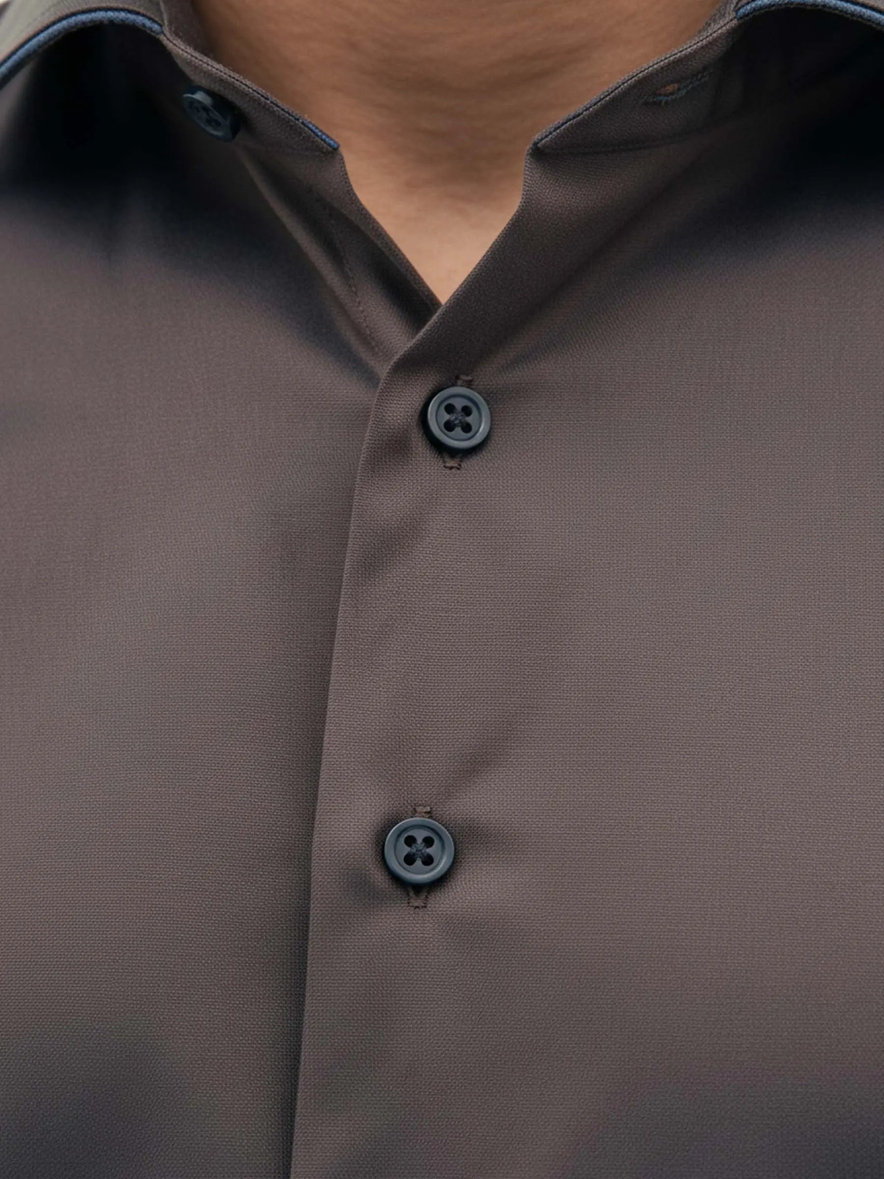 Detail view of light brown men’s shirt with contrast buttons and modern collar.