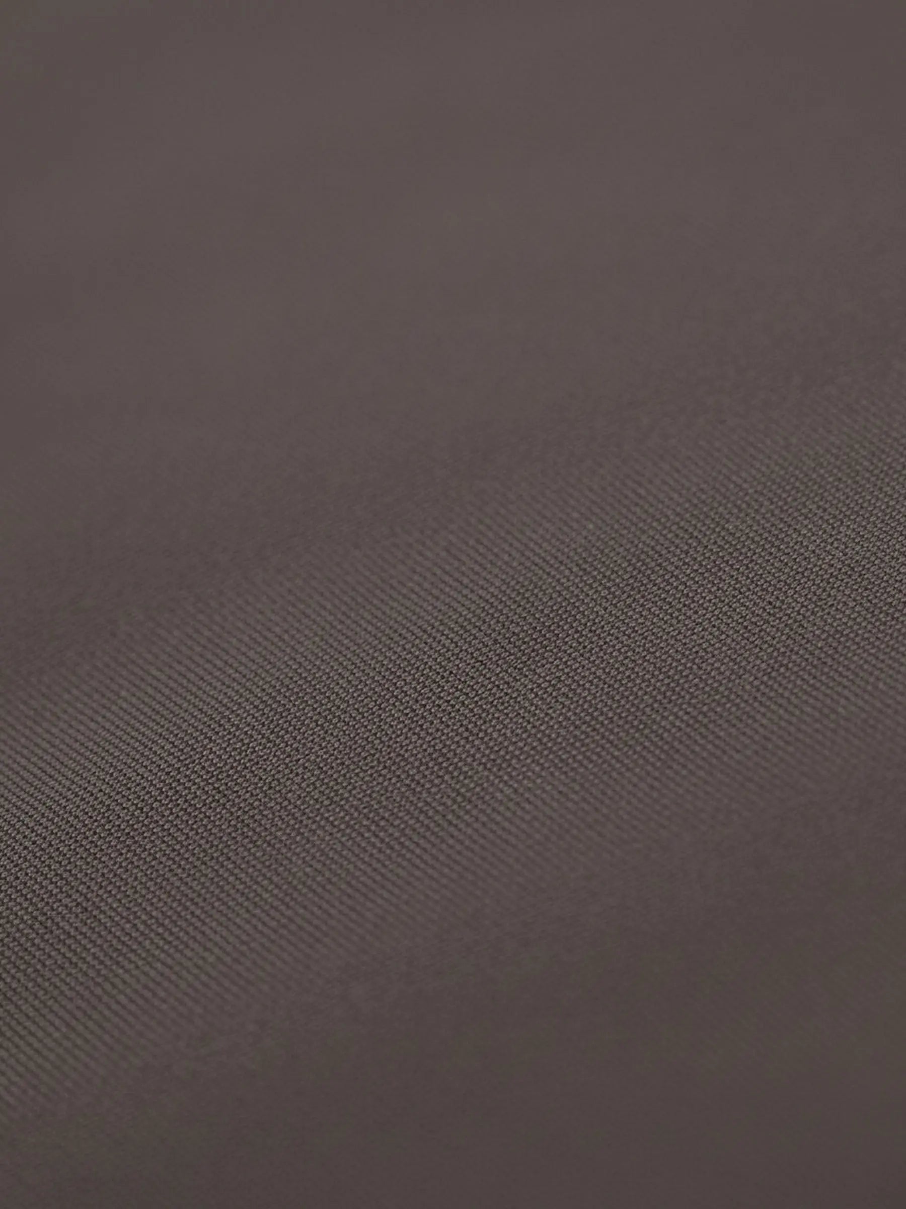 Close-up of light brown shirt fabric with smooth texture and fine weave.