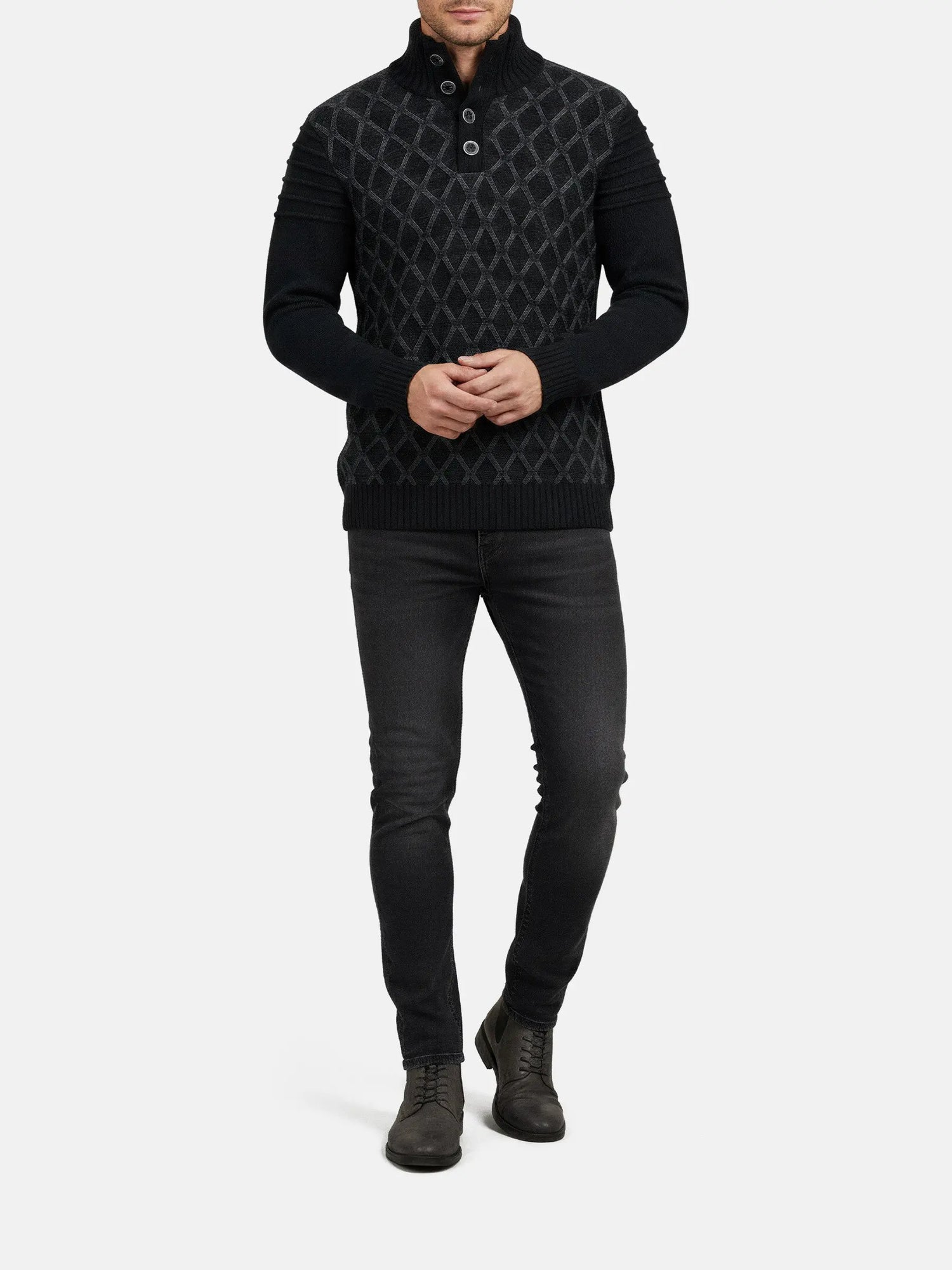 Full-body view of a man wearing an anthracite textured knit sweater with dark jeans.