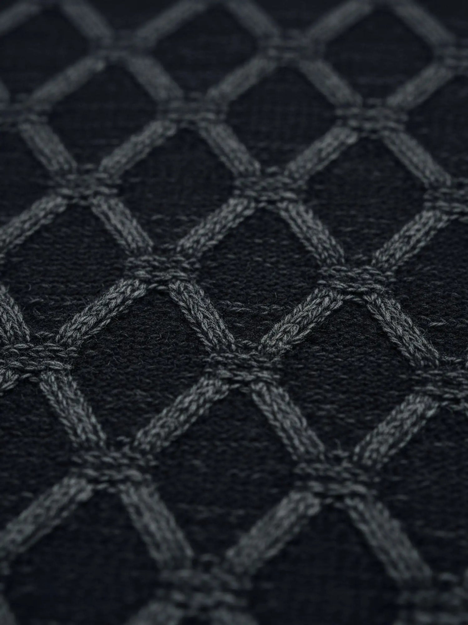 Close-up of anthracite knit sweater fabric featuring a raised geometric diamond pattern.