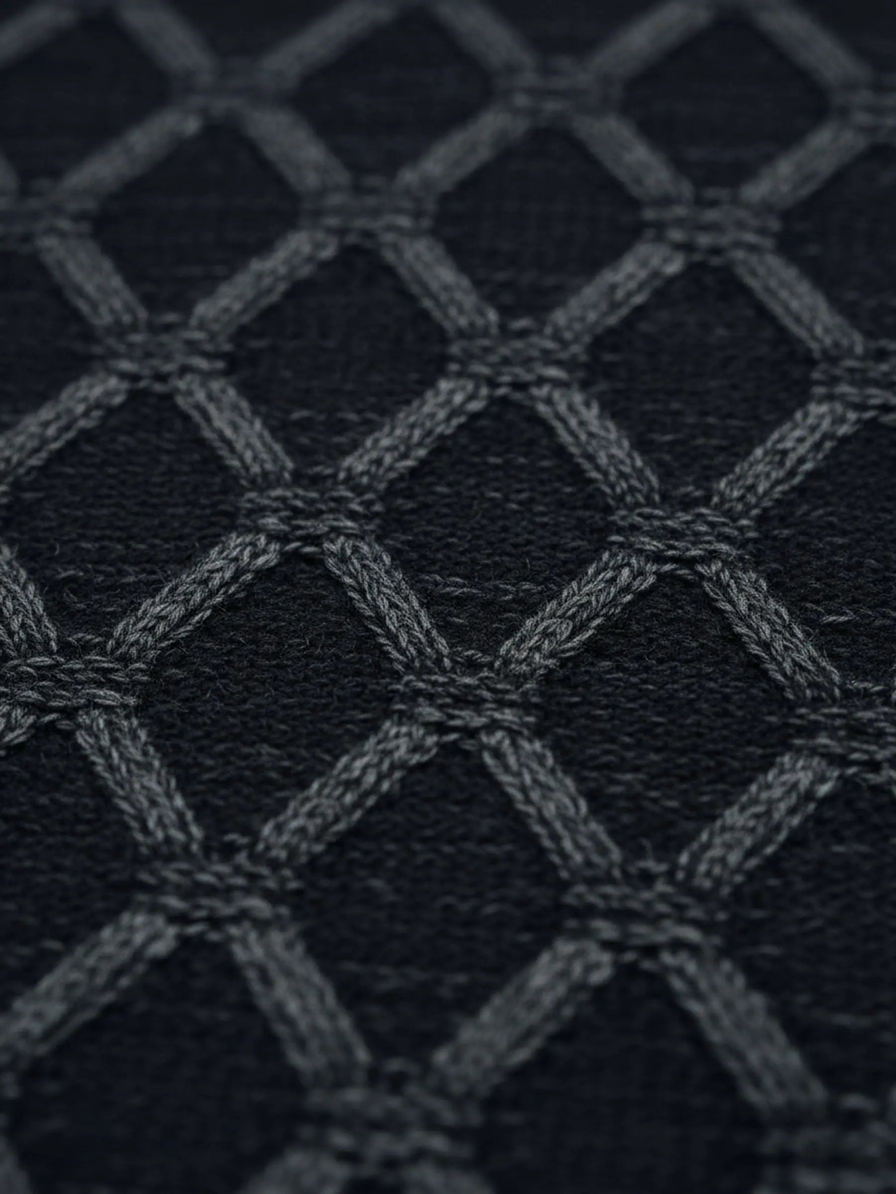 Close-up of anthracite knit sweater fabric featuring a raised geometric diamond pattern.