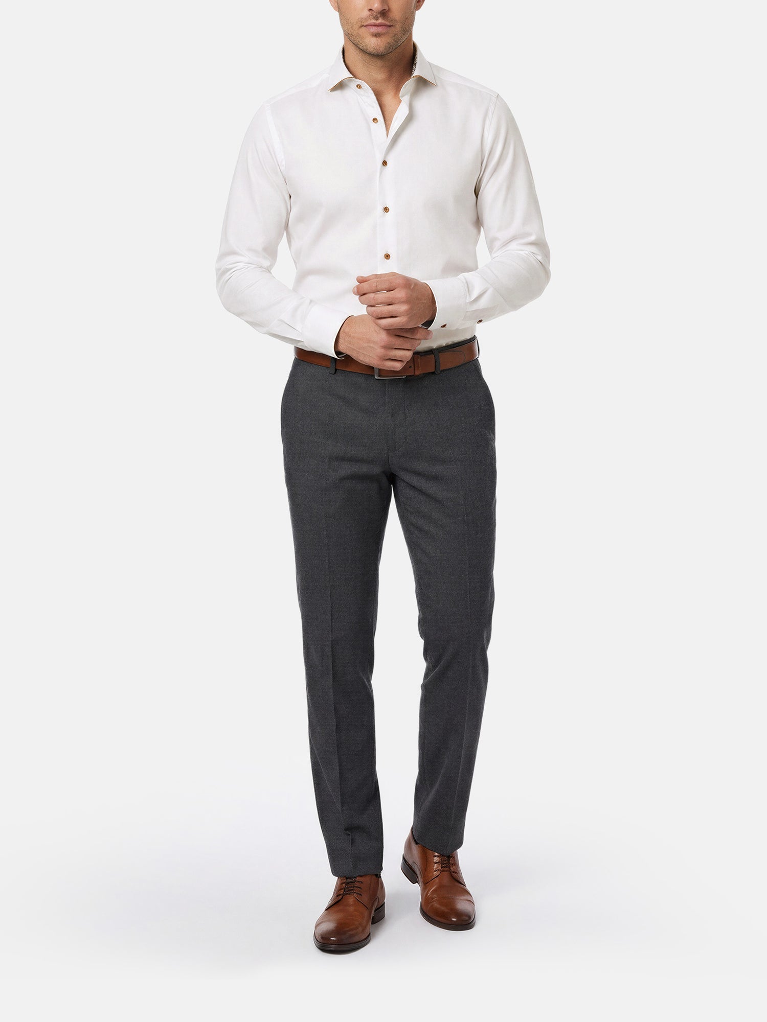Model wearing men’s white dress shirt styled with grey trousers and brown leather shoes.