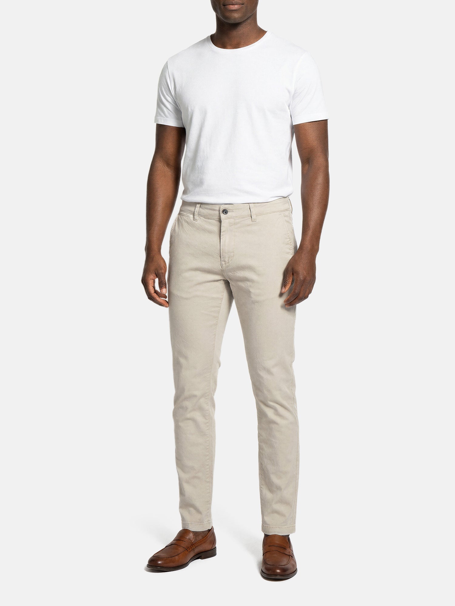 Model wearing light beige slim-fit men’s chino pants styled with white t-shirt.