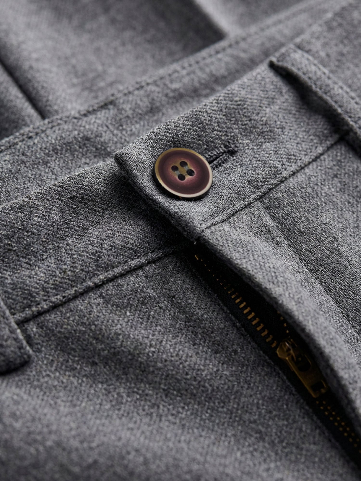 Close-up of grey pantalon fabric showing button detail and zip fastening for tailored trousers.