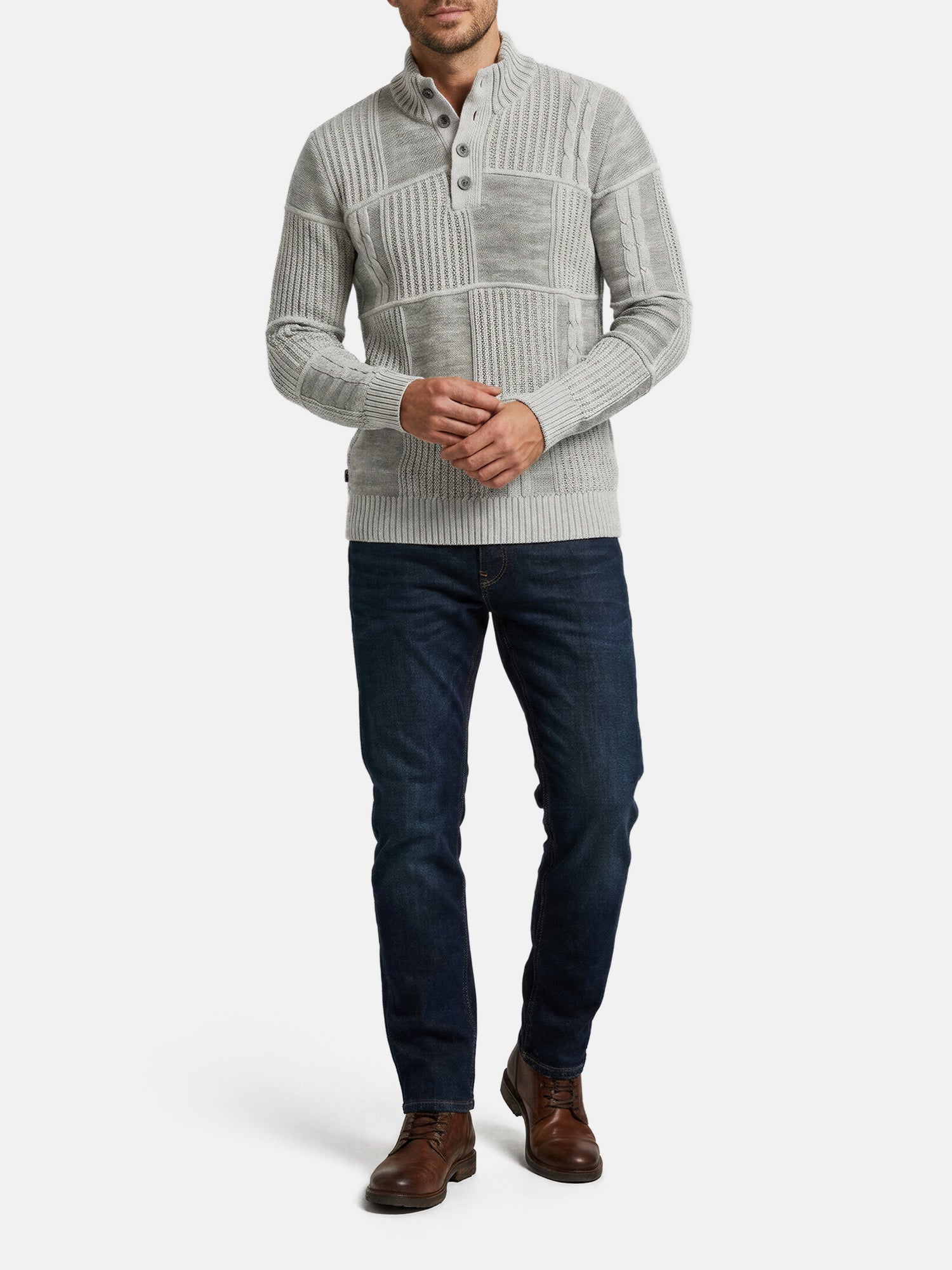 Man wearing light grey knit sweater with textured panels, paired with dark jeans and boots.