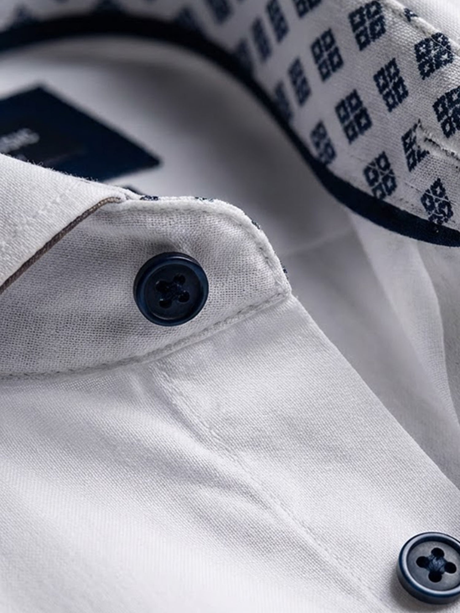 Close-up of white men’s dress shirt with navy buttons and patterned collar lining