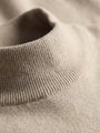 Close-up of beige pullover’s ribbed mock-neck fabric texture.