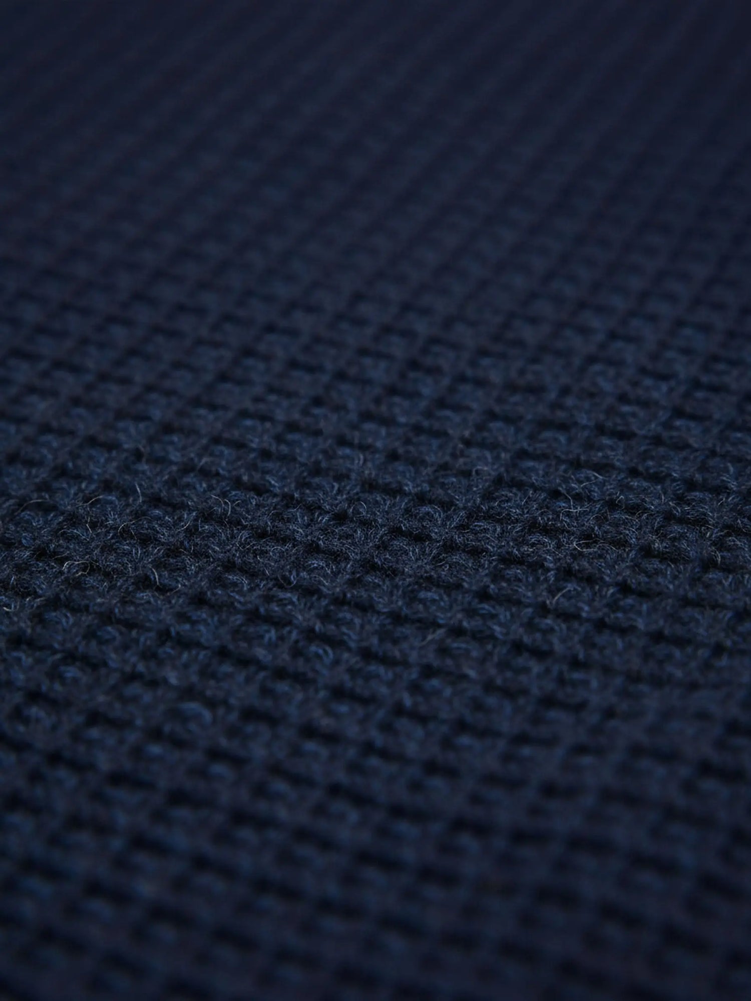 Close-up of indigo navy knit fabric showing dense textured waffle pattern.