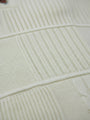Close-up of off-white knit sweater fabric showing textured ribbed and patterned details.