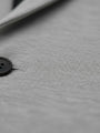 Close-up texture of light grey blazer fabric with button detail.