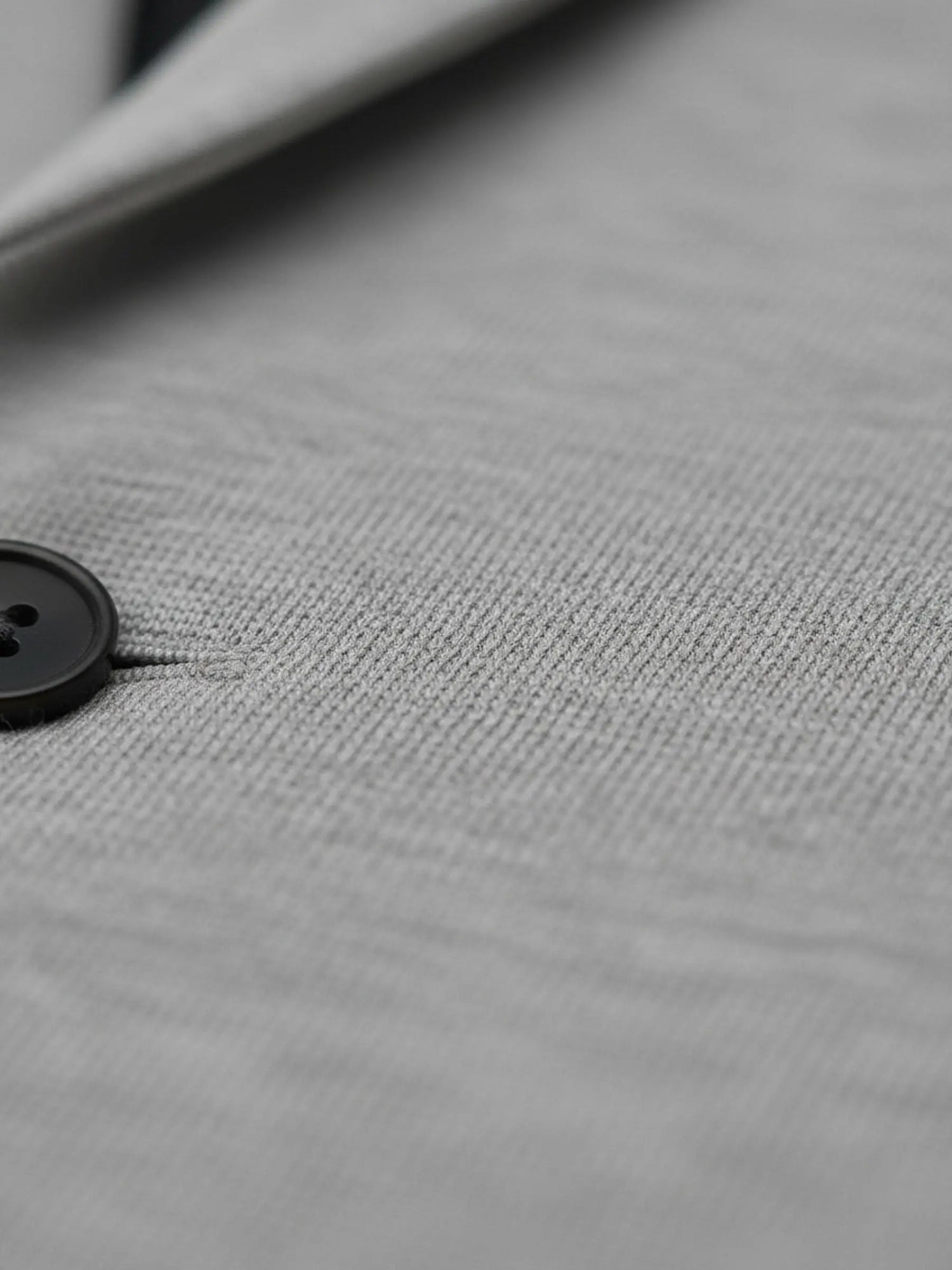 Close-up texture of light grey blazer fabric with button detail.