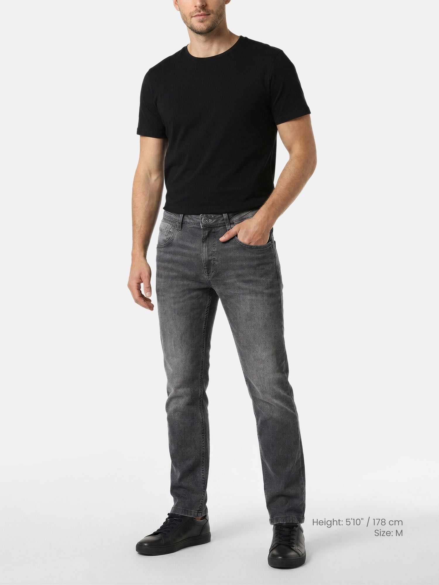 Model wearing grey slim fit jeans with black t-shirt and sneakers.